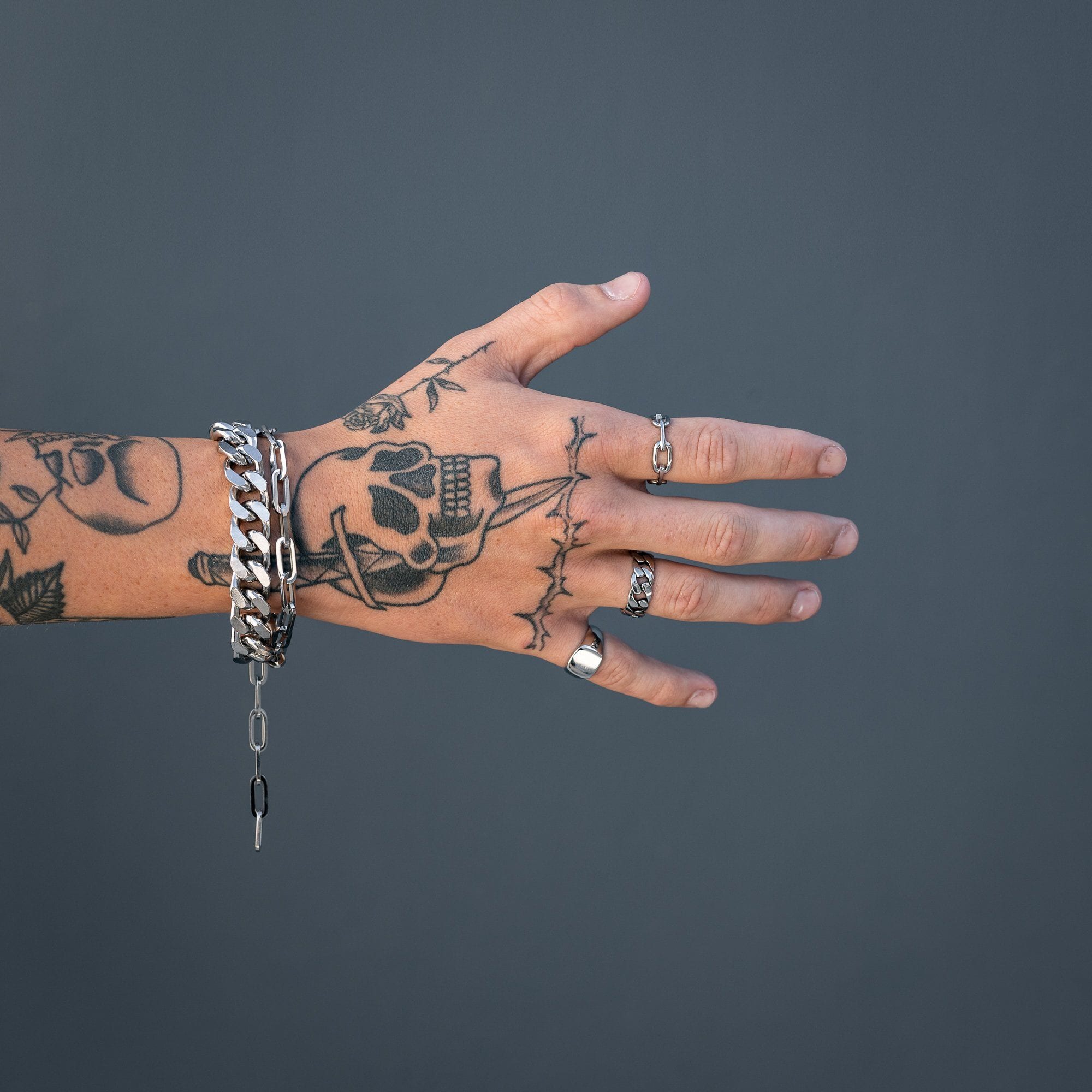 tattooed hand with cuban link cluster bracelet against blue wall