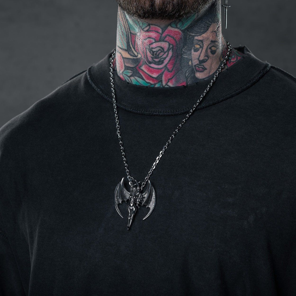 man with tattooed neck and black shirt wearing succubus pendant on long chain
