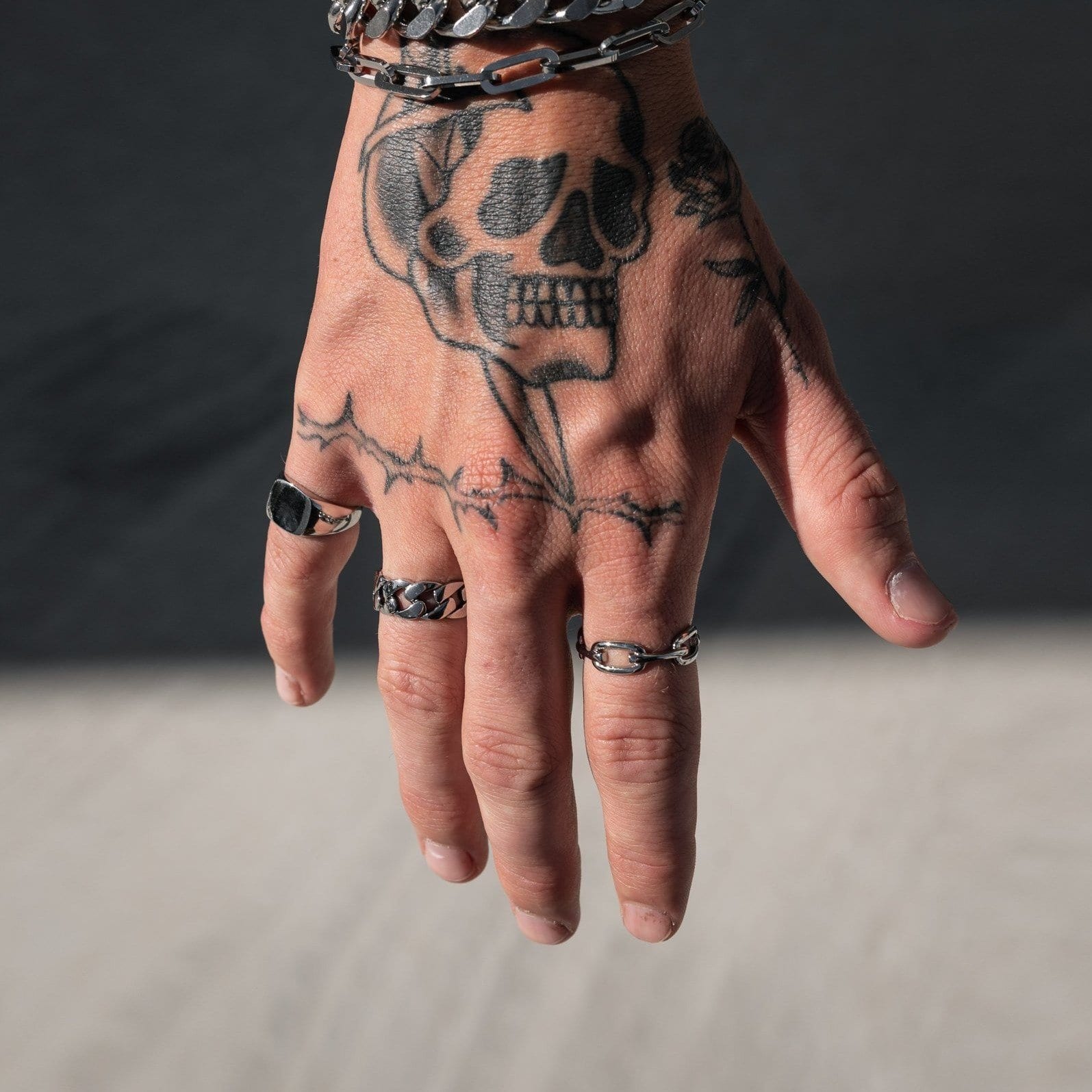 tattooed mens hand showing silver rings on cement background