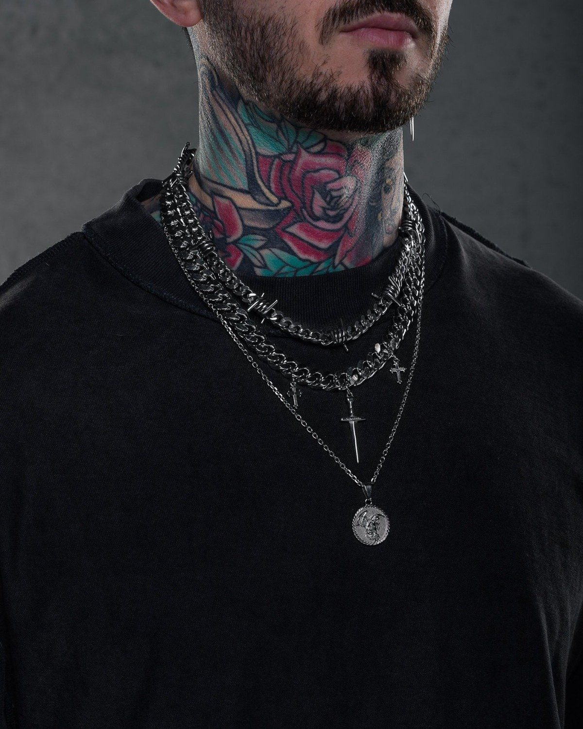 tattooed man wearing layered statement necklace chains with spikes and daggers