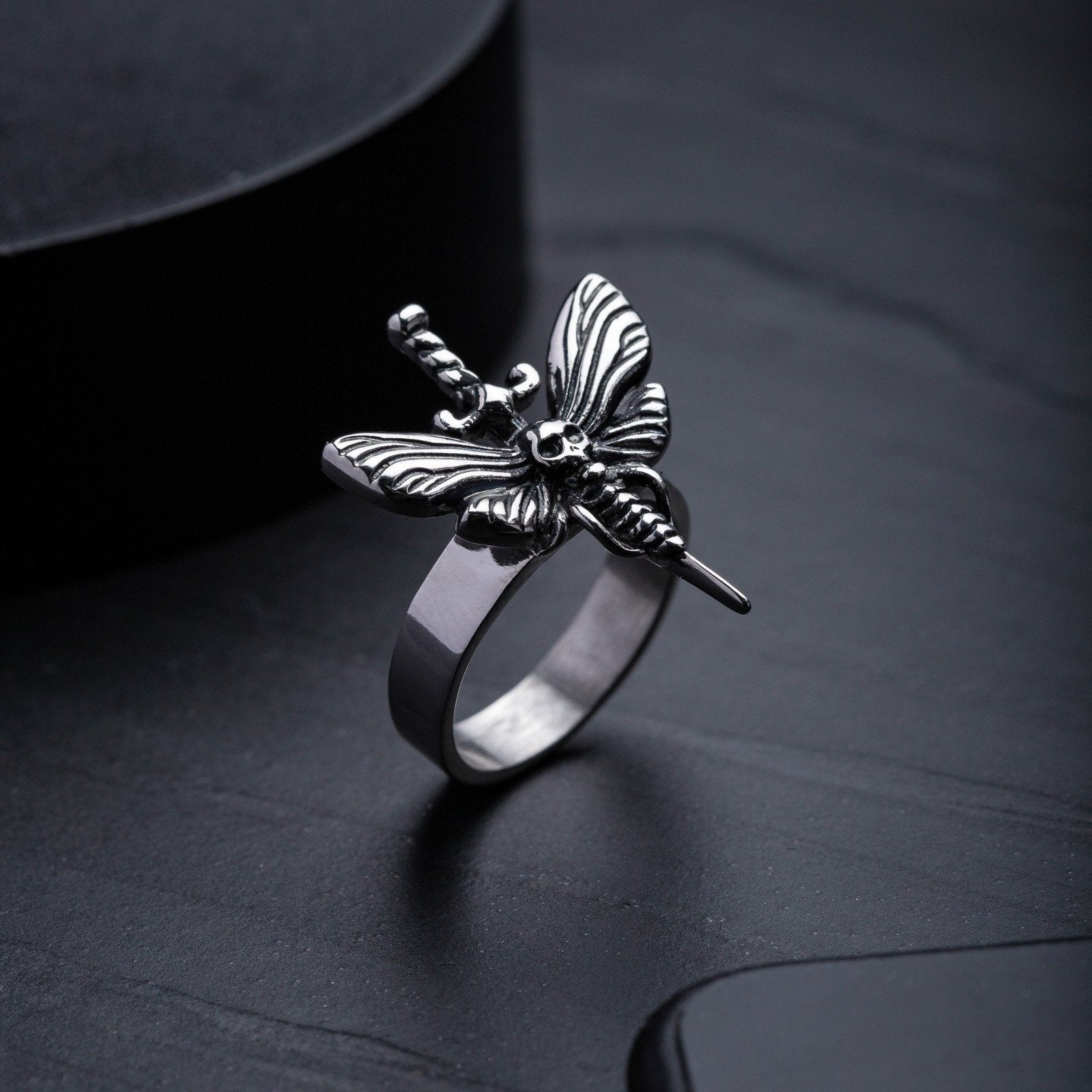 Moth ring with dagger in stainless steel on dark stone background by statement collective