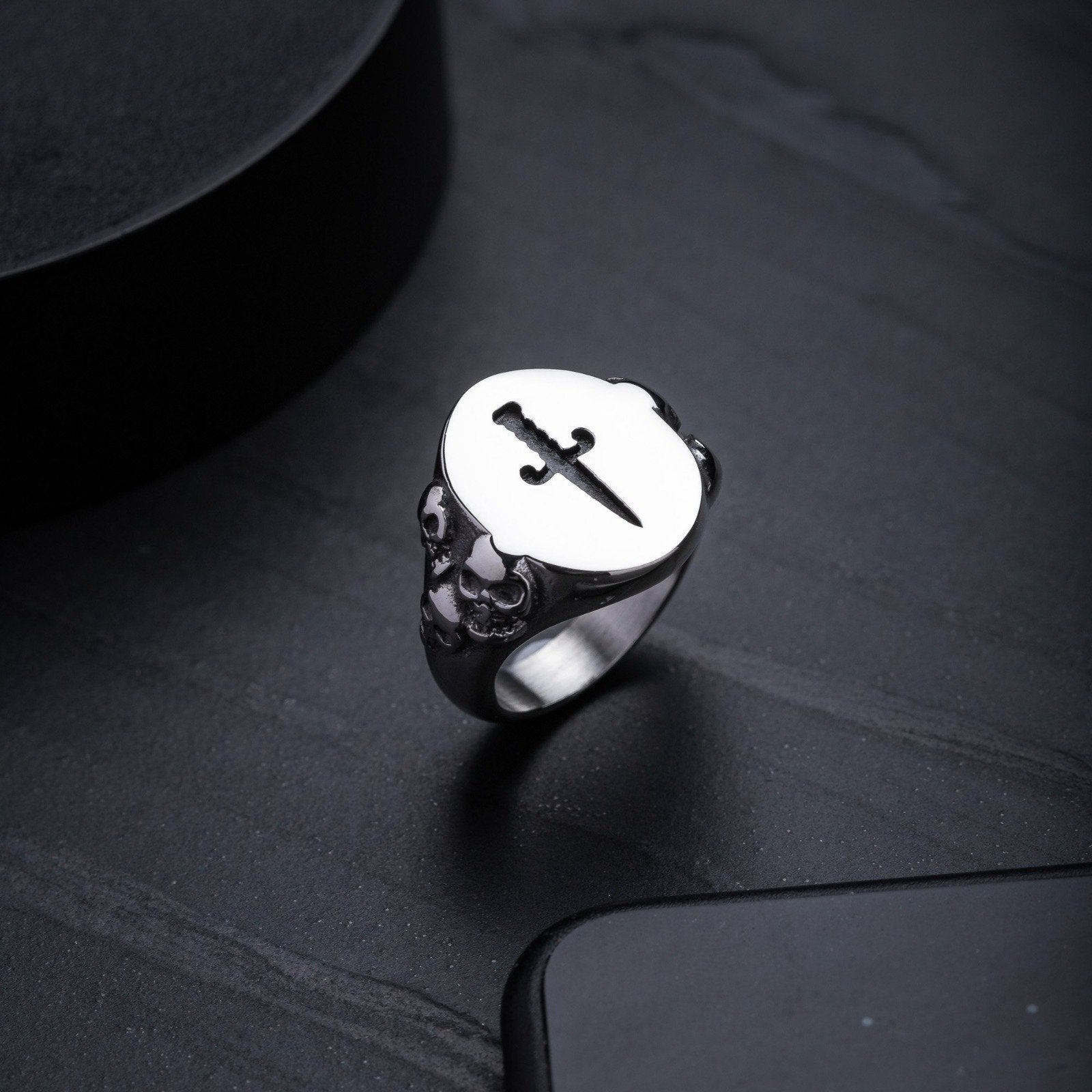 mens signet ring with skull designs on the side on dark stone background by statement collective