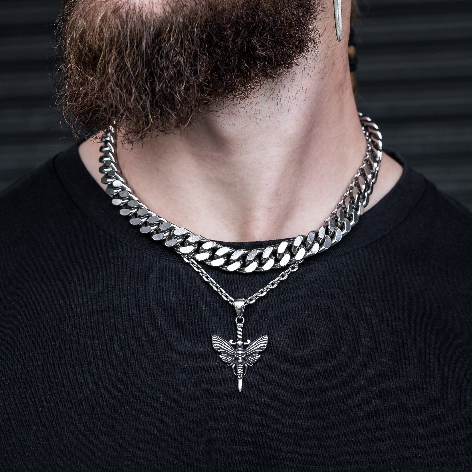 A bearded person wears a 13mm Chunky Cuban Chain and a silver moth pendant necklace, paired with a black shirt.