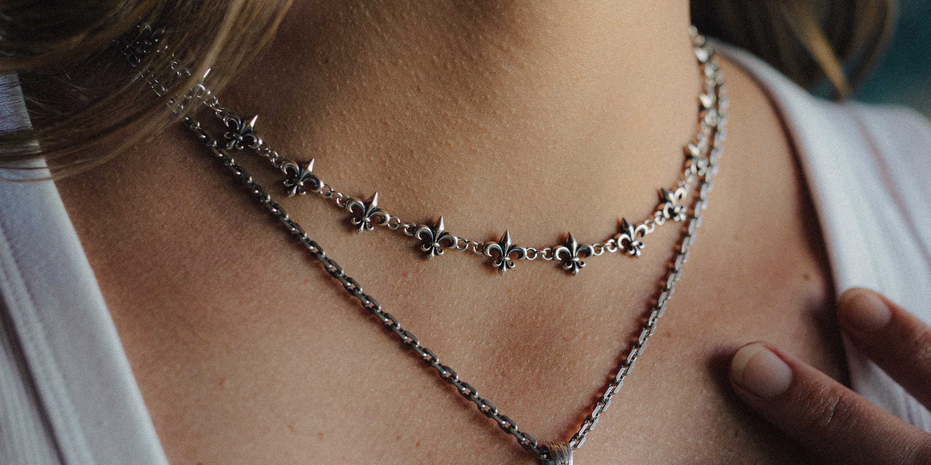 Close-up of a person wearing layered necklaces: one with white pearls and two with chunky silver chains, all against a black top.