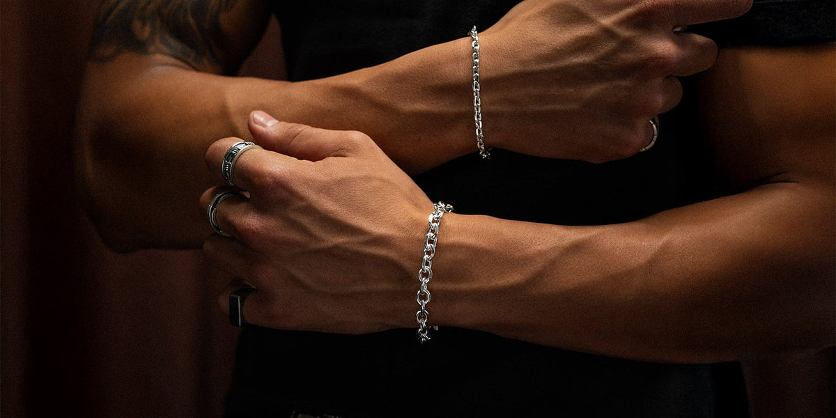 man with black shirt wearing bright sterling silver bracelets by statement collective against brown background