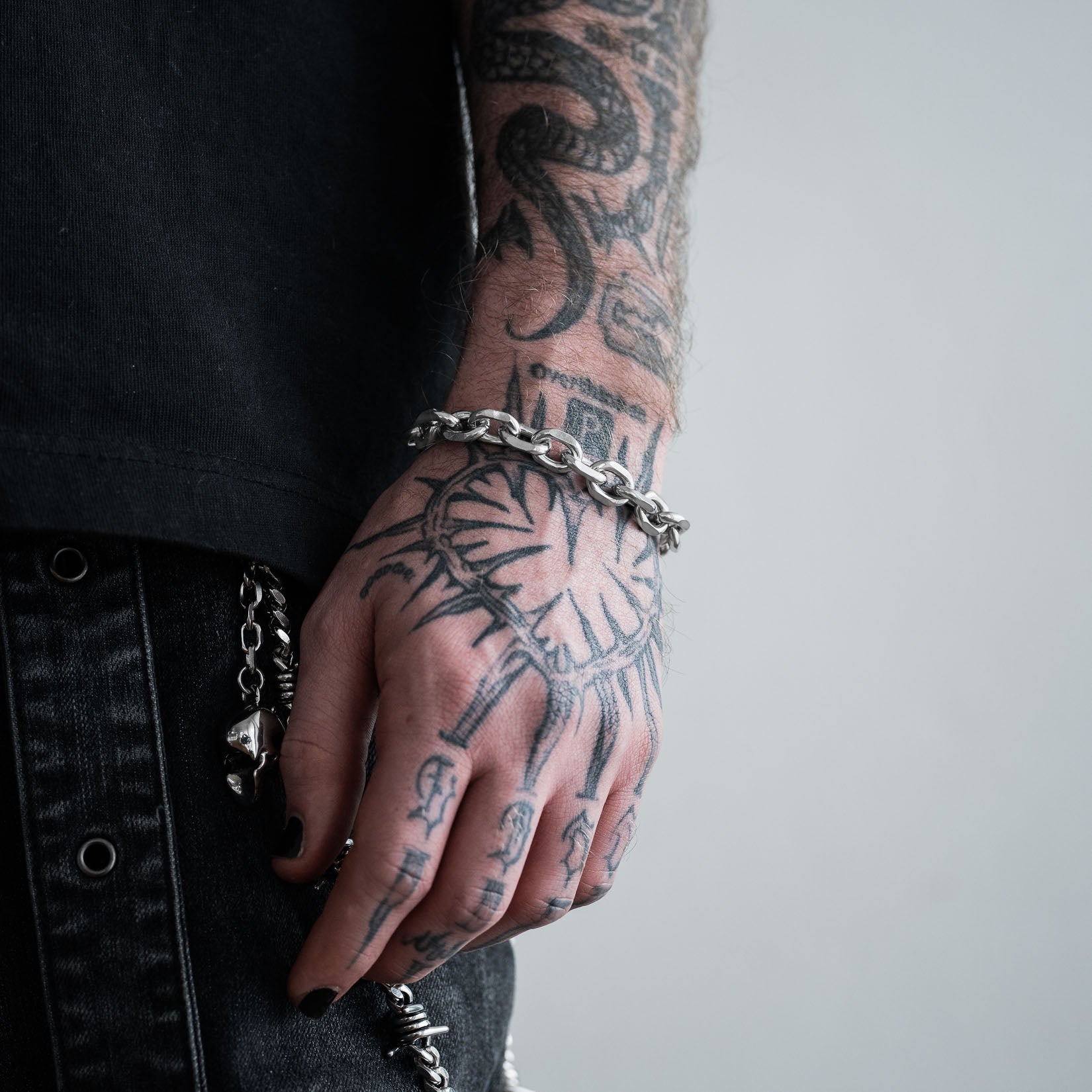 Tattooed arm with a 10mm cable chain bracelet on a plain background