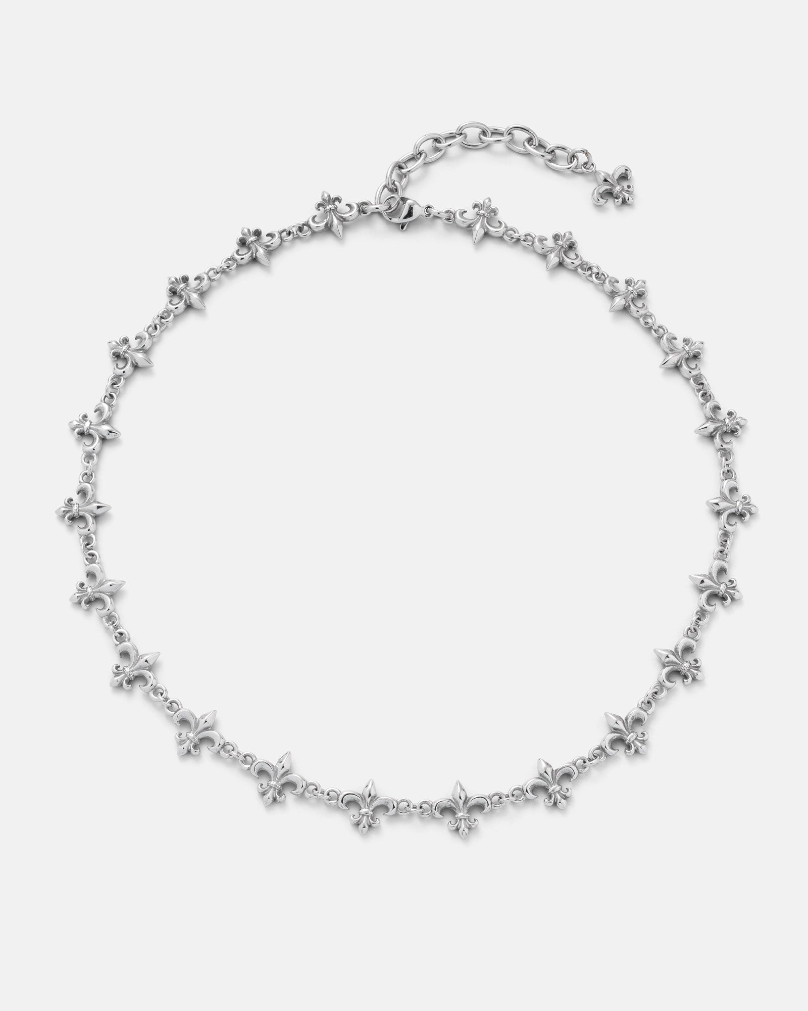 The "Fleur De Lis" 10mm Chain by Statement Collective is a silver necklace adorned with multiple evenly spaced small fleur-de-lis charms along the chain, finished with an adjustable clasp and an extra fleur-de-lis charm at the end of the extender.