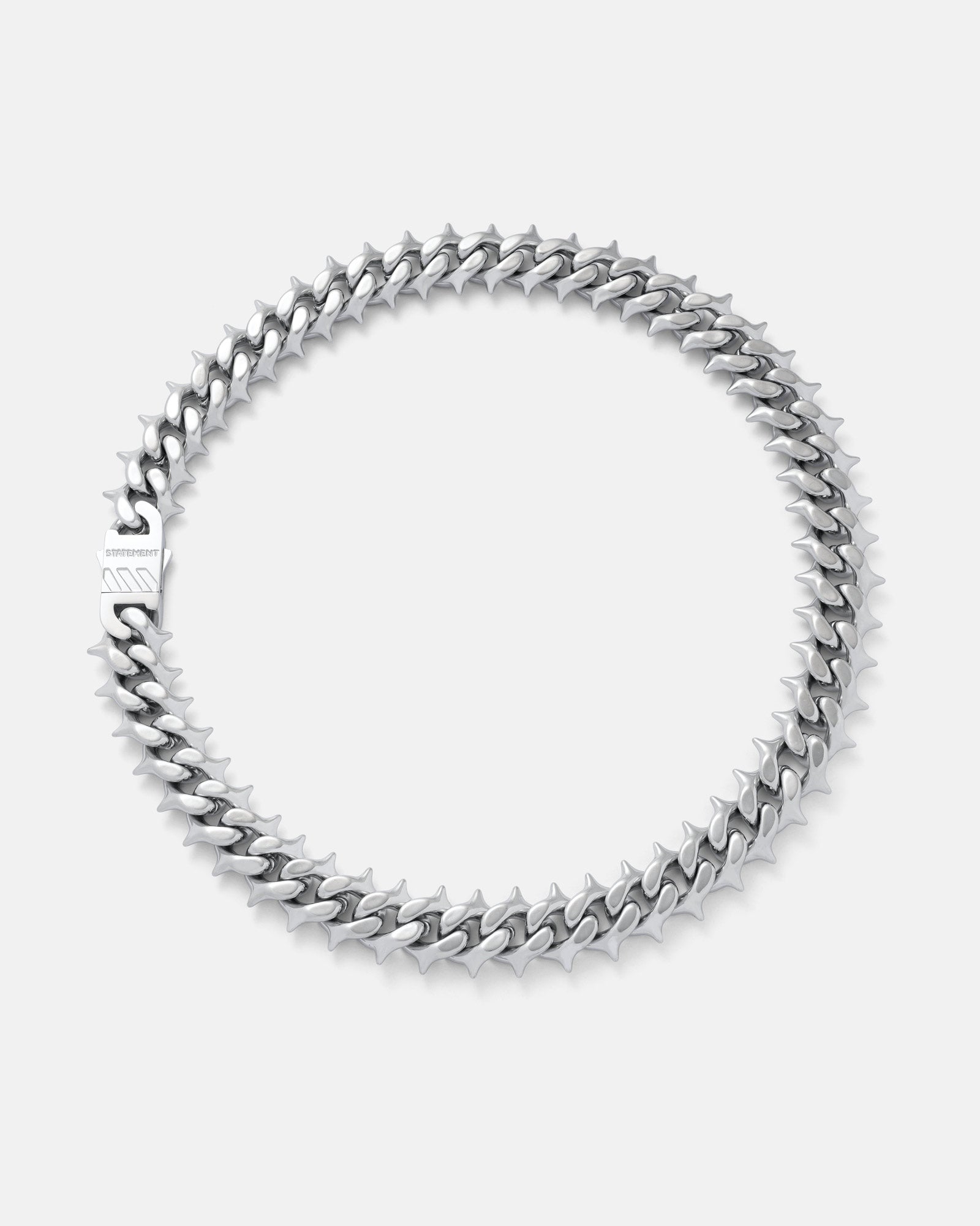 The "Chainsaw" Spiked Cuban Chain, a silver stainless steel necklace with interlocking links and clasp, is displayed in a circular shape on a plain light gray background.