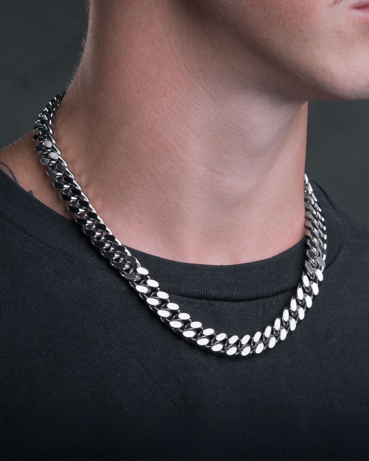 A close-up of a person wearing the 11mm Cuban Chain over a black shirt, highlighting the neck and lower face with a dark, blurred background.