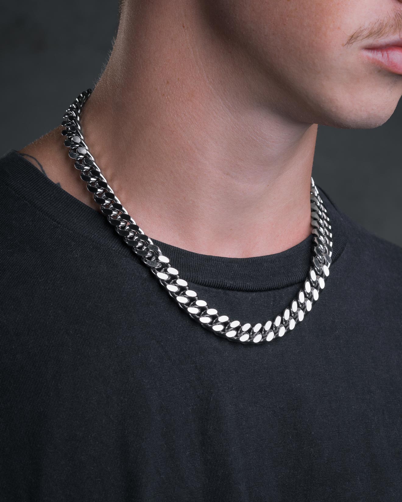 A close-up of a person wearing a black shirt and the 11mm Cuban Chain necklace, showing only the lower half of their face and neck against a dark background.