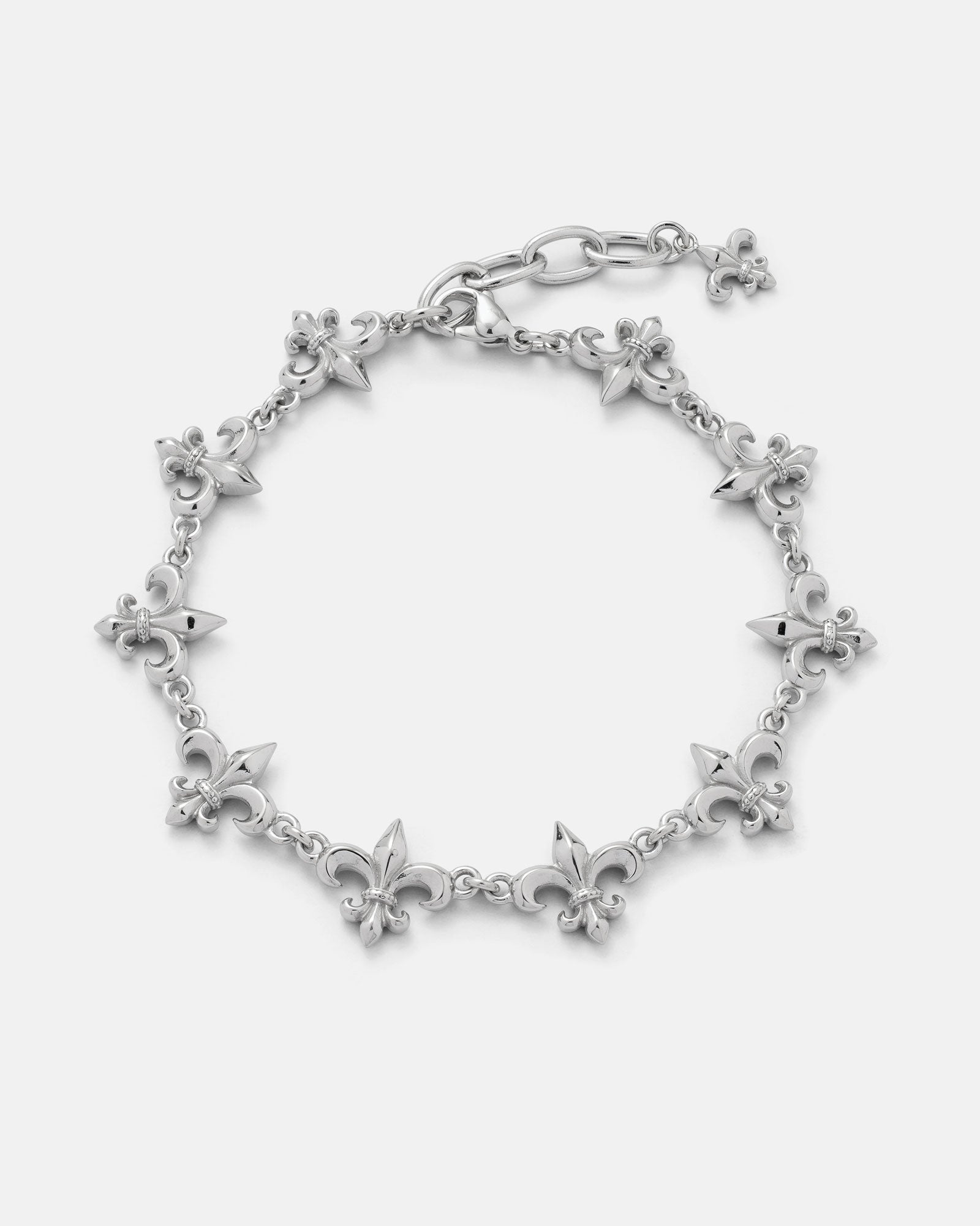 The "Fleur De Lis" 15mm Bracelet by Statement Collective showcases a silver design with alternating fleur-de-lis and pointed spike charms, finished with a lobster clasp and a small dangling fleur-de-lis charm at the end.