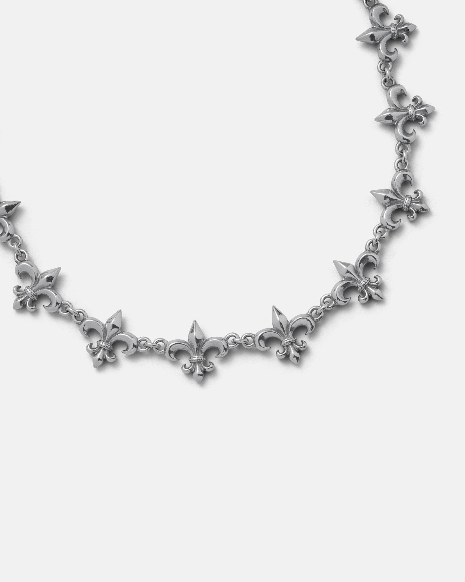 The "Fleur De Lis" 15mm Chain by Statement Collective showcases multiple silver fleur-de-lis pendants linked together in a repeating pattern, displayed against a plain white background.