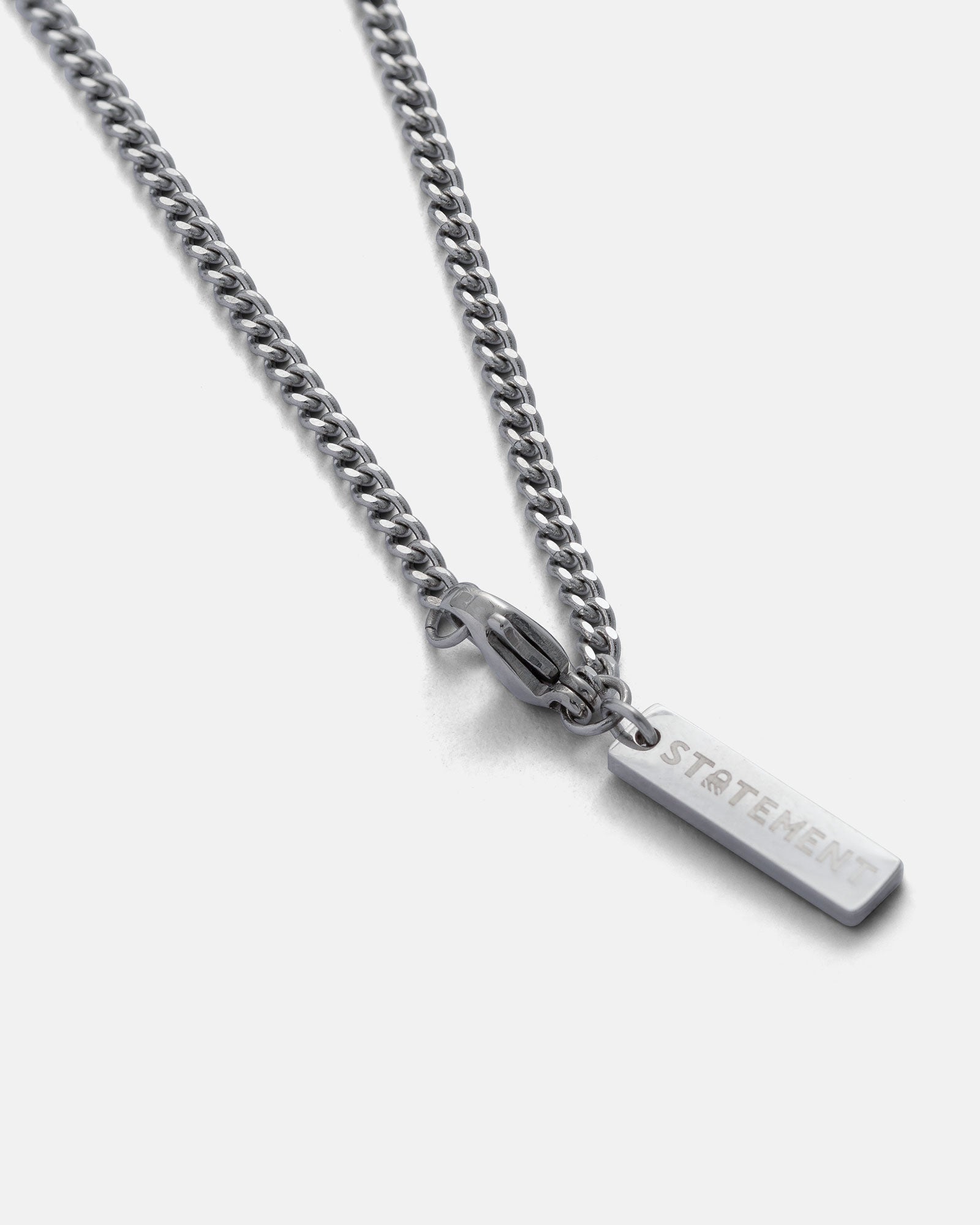 A 2.3mm curb chain necklace with a rectangular pendant engraved with the word STATEMENT, displayed on a plain light gray background.