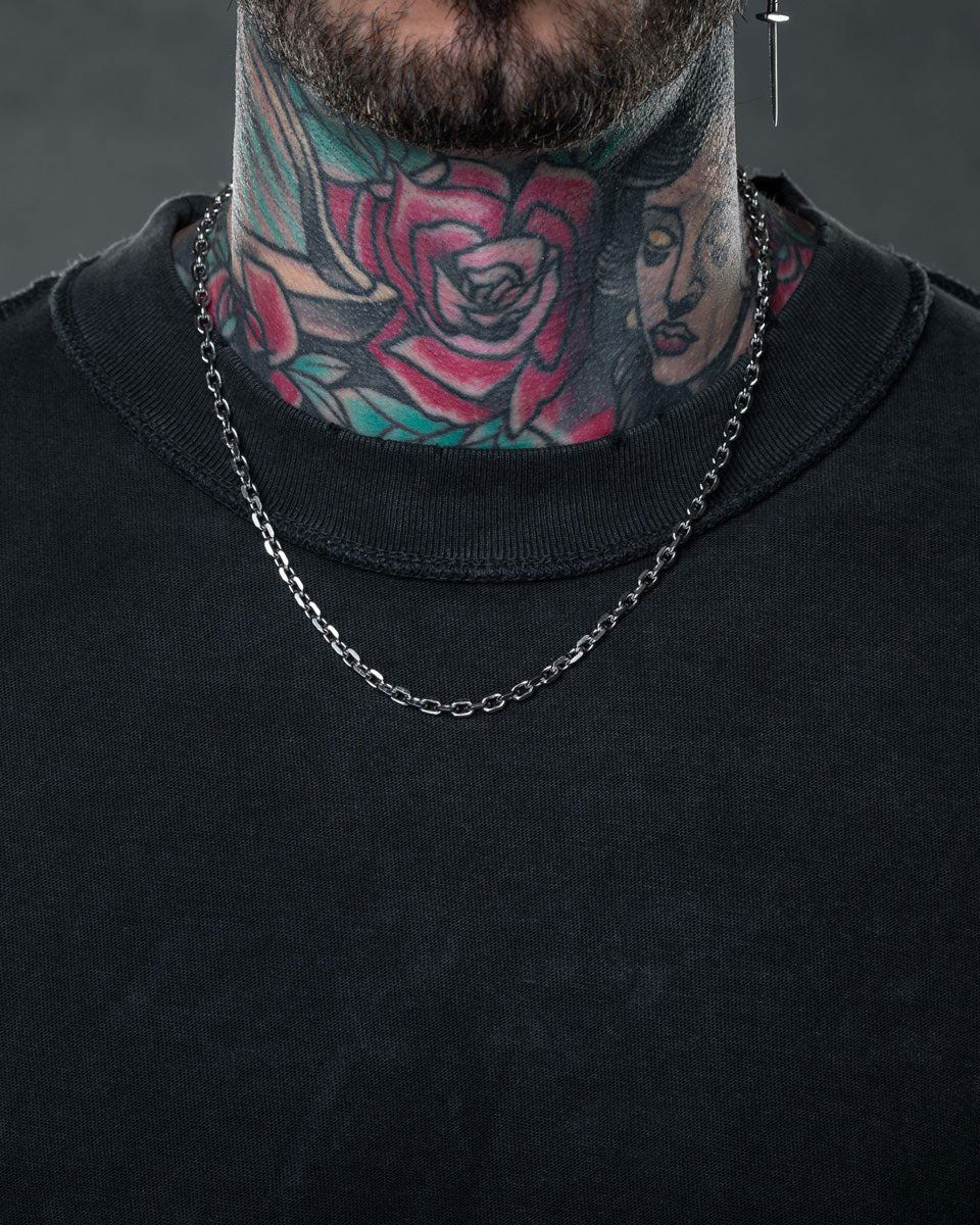 A person in a black shirt and Statement Collective’s 4.5mm Cable Chain necklace has colorful rose and woman’s face tattoos on their neck, with only the lower face and neck visible.