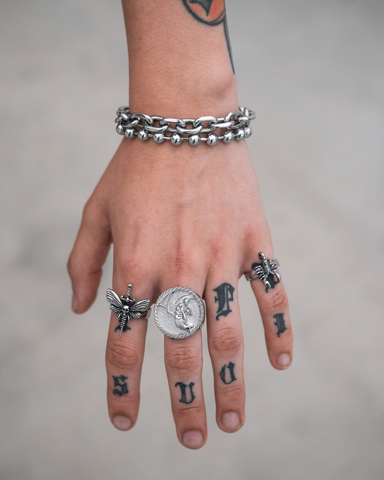 A tattooed hand with "SLOW" on the knuckles wears a 7mm Ball Bracelet and three silver rings—a coin ring and two with bee motifs—for a bold 90s vintage vibe.