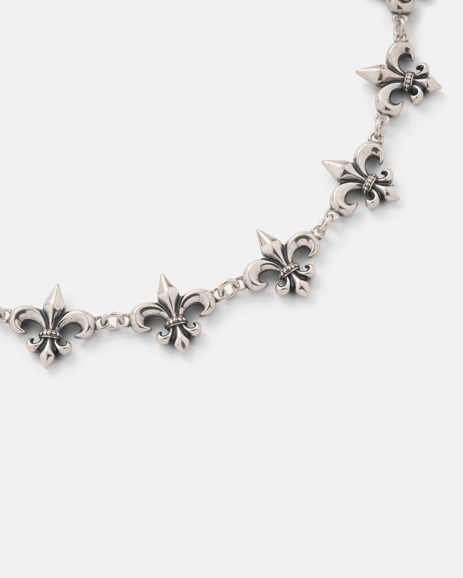 A 925 sterling silver "Fleur De Lis" 15mm chain by Statement Collective, showcasing multiple interconnected fleur-de-lis pendants in a partial arc against a plain white background.