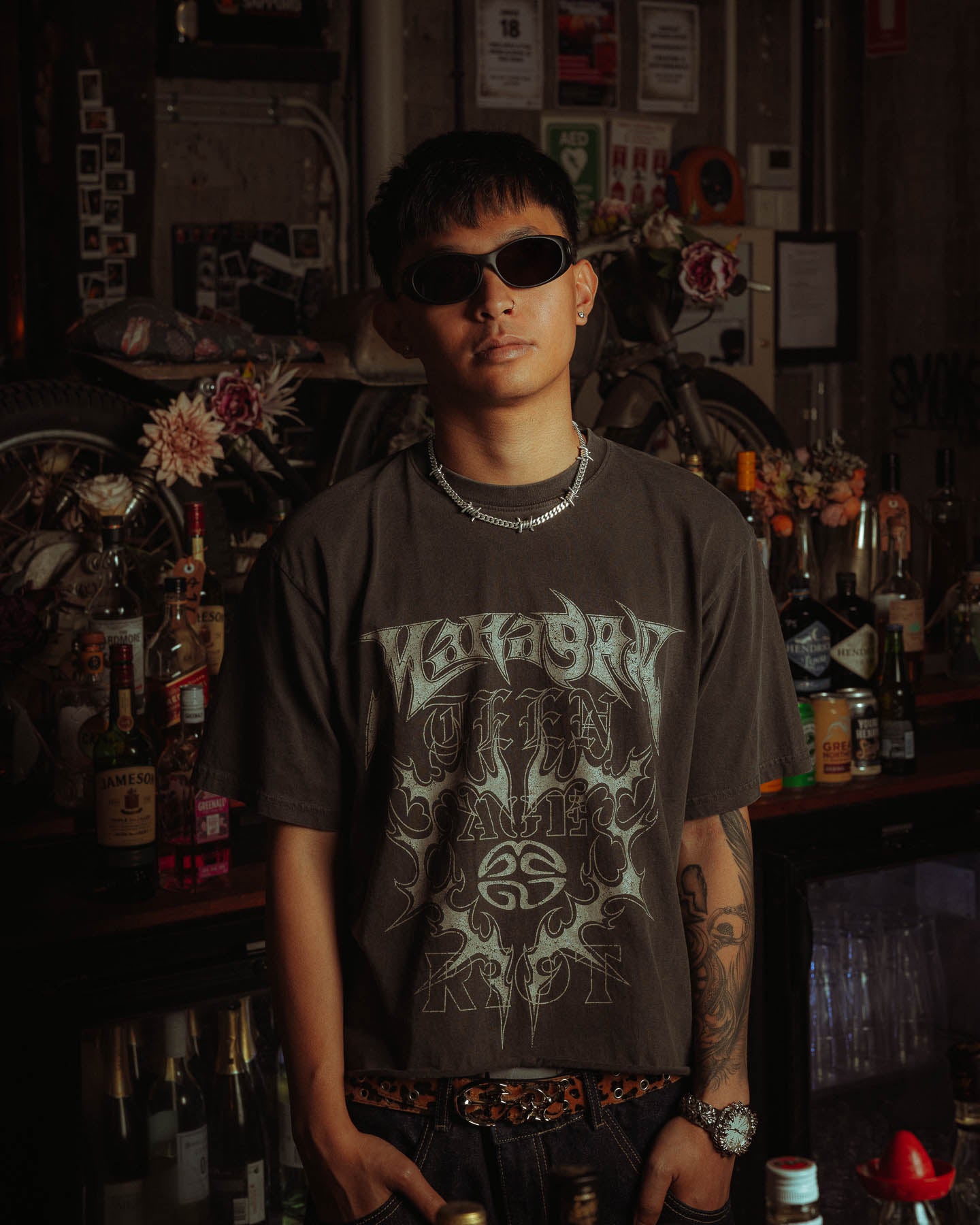 male model standing with hands in pockets, with the mm barbed wire chain in sterling silver sitting around his neck, standing in front of decorated background 