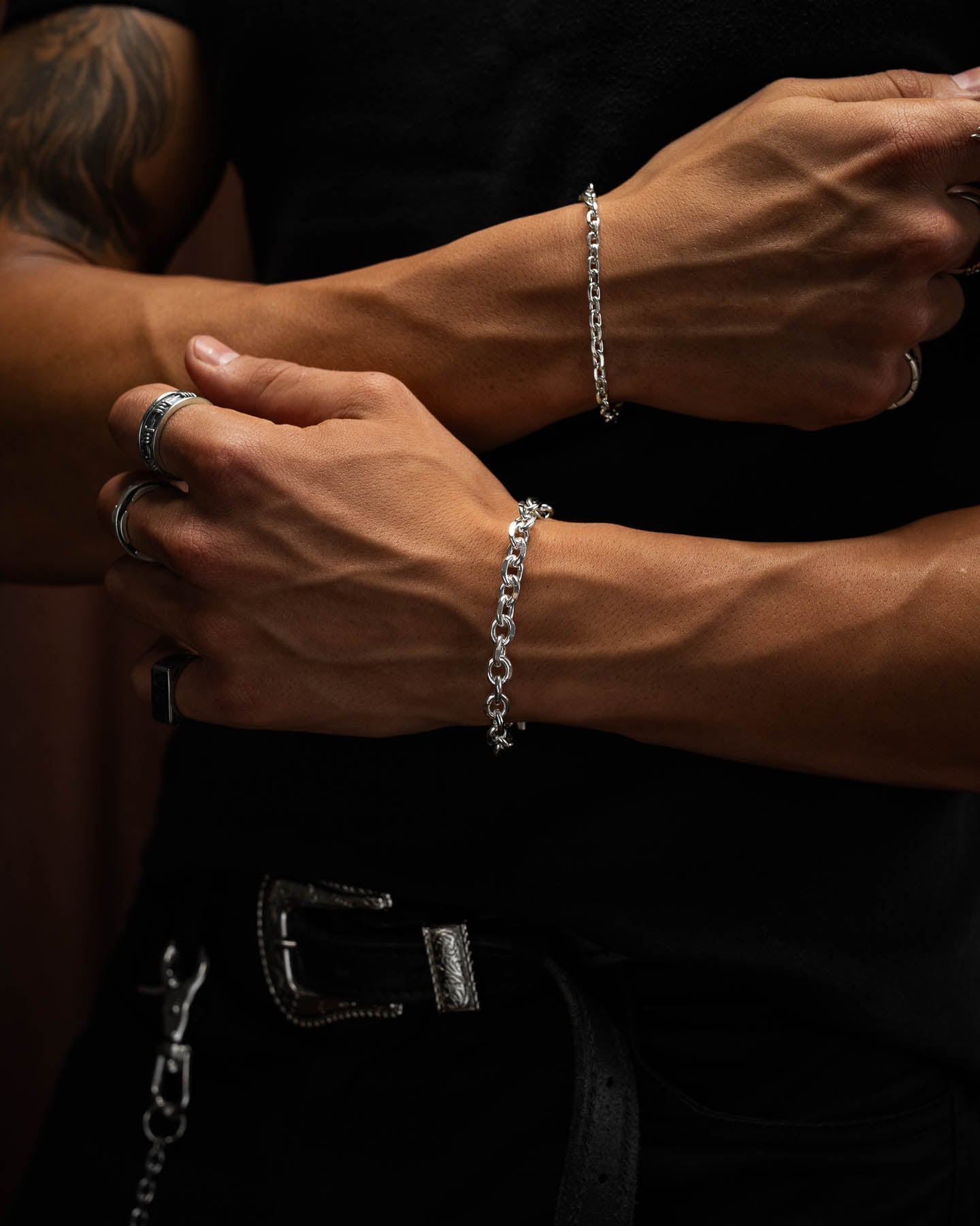 male model arms crossed over his black shirt,  showing the 8mm cuban link bracelet in 925 sterling silver. against brown velvet backdrop.