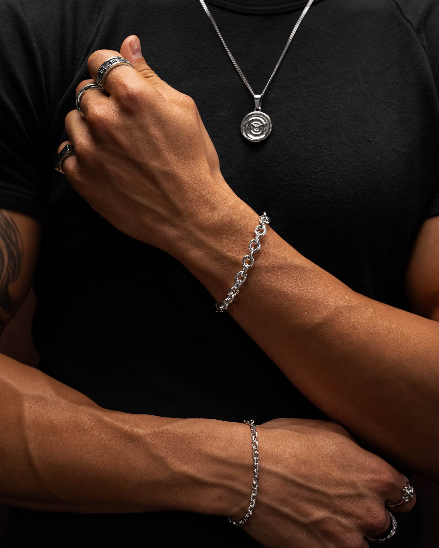 male model arms crossed over his black shirt  showing the 4.5mm and the 8mm cuban link bracelets in 925 sterling silver.