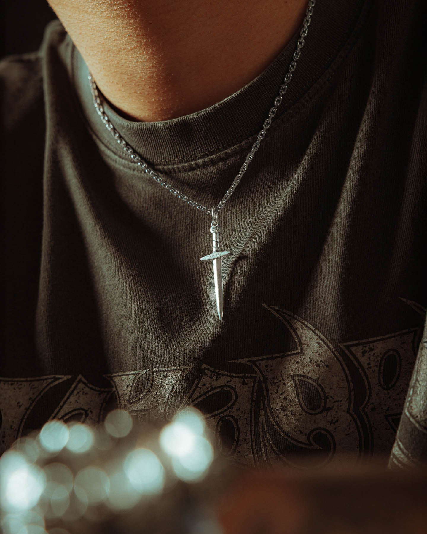 A person in a dark shirt wears the 925 Sterling Silver Dagger Pendant necklace; the photo highlights the jewelry’s .925 silver finish and part of the shirt's graphic design.
