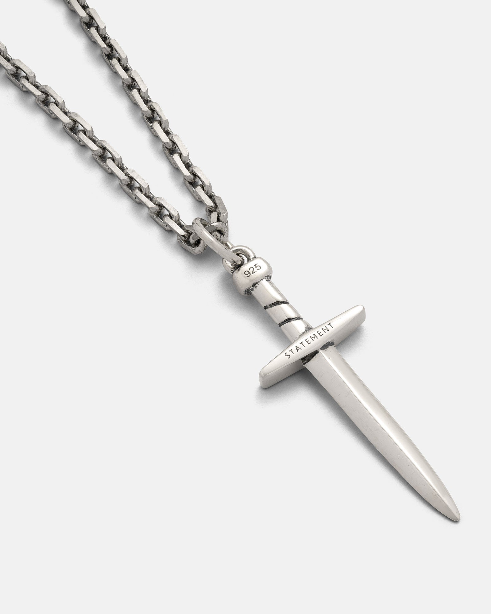 The 925 Sterling Silver Dagger Pendant features a detailed silver dagger on a chain, engraved with "STATEMENT" on the crossguard and stamped "925" on the hilt, shown against a plain white background.