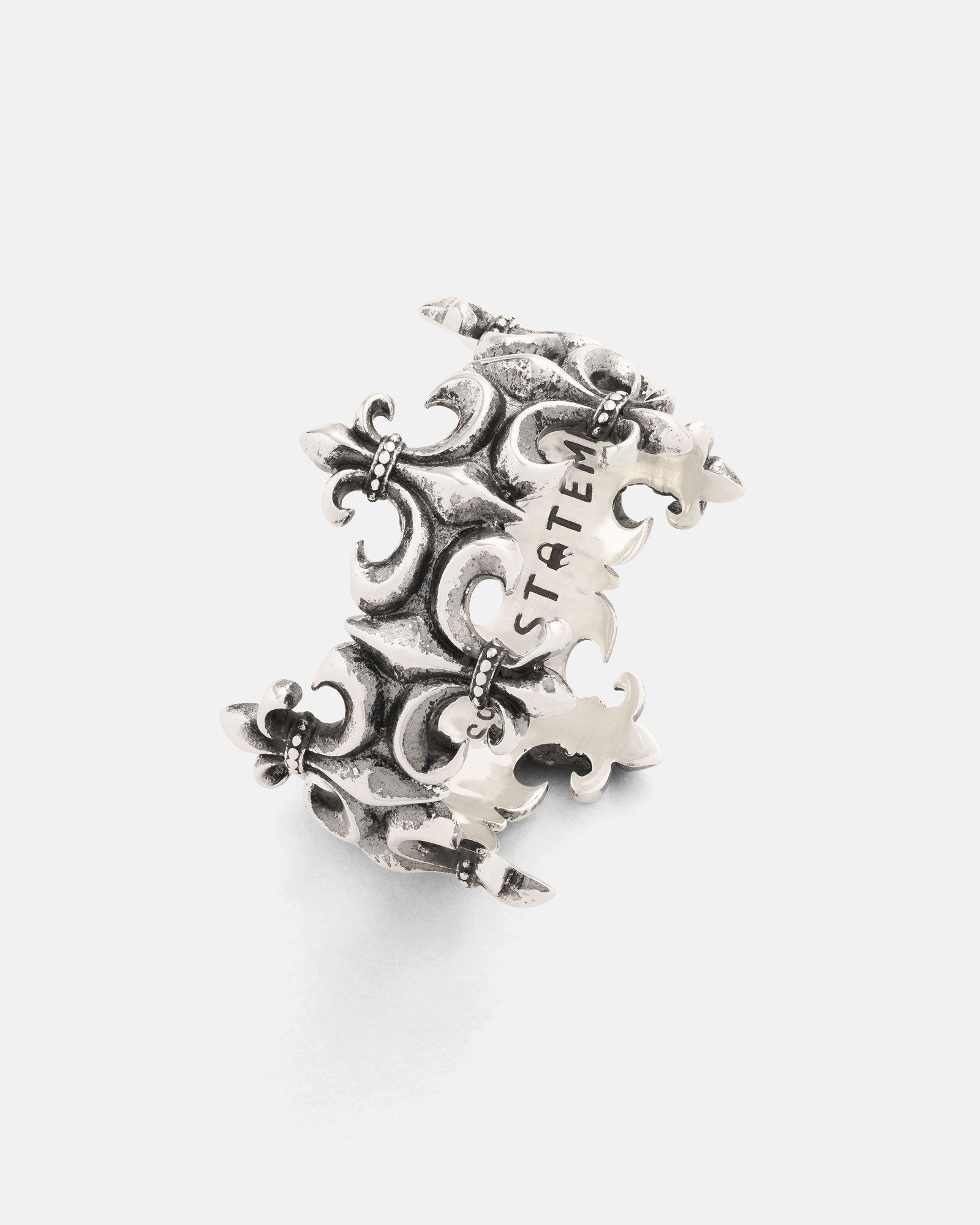 Crafted by Statement Collective, the 925 Sterling Silver “Crested” Fleur De Lis Ring boasts an intricate fleur-de-lis design and a textured antique finish that enhances its timeless charm. The band is engraved with STATEM in bold uppercase letters, blending classic elegance with modern statement style.