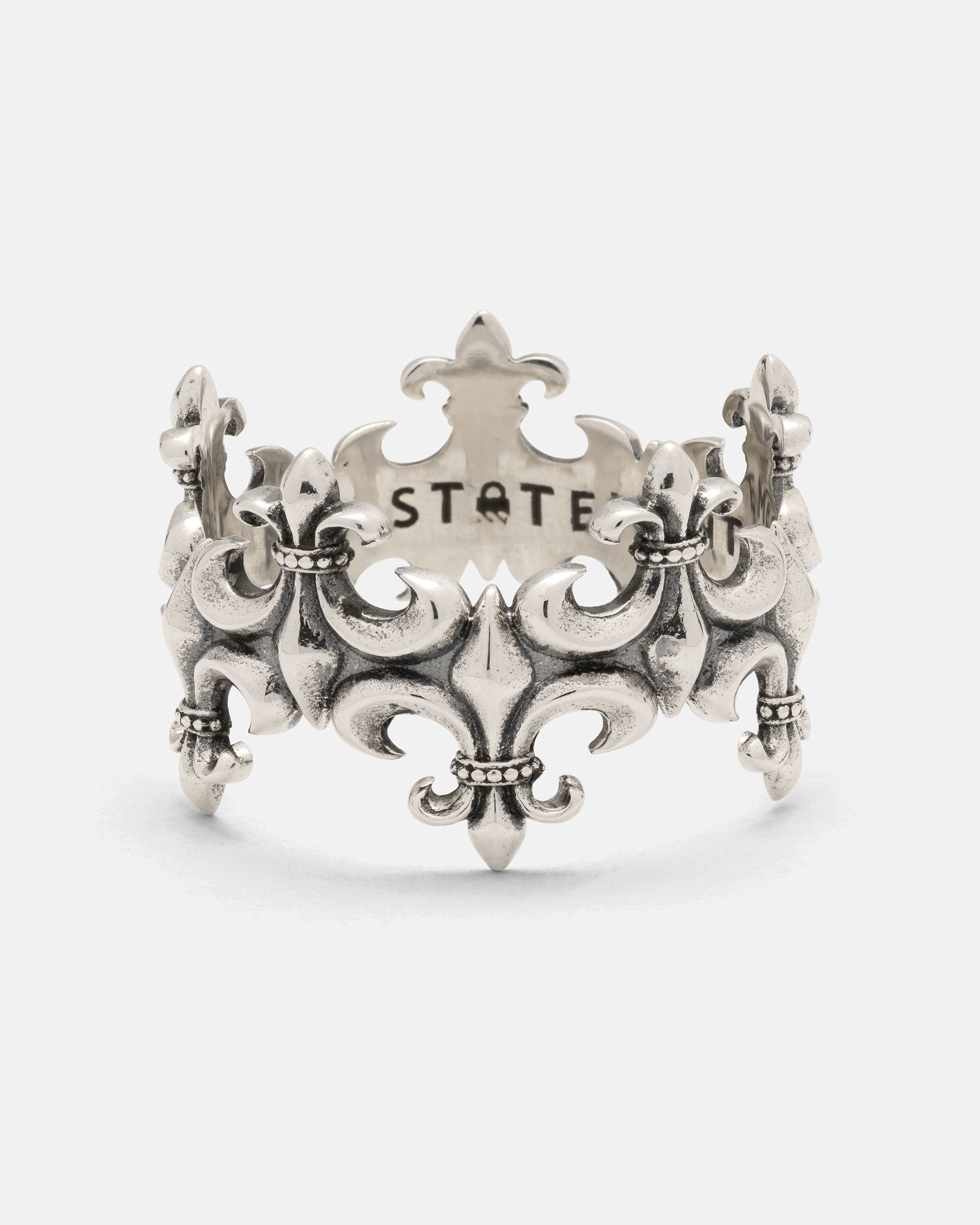925 Sterling Silver “Crested” Fleur De Lis Ring by Statement Collective: This vintage-inspired ring showcases intricate fleur-de-lis motifs and elegant openwork detailing. Expertly crafted from 925 Sterling Silver, it features the word STATE engraved on the inner band and is finished with a timeless, antique patina.