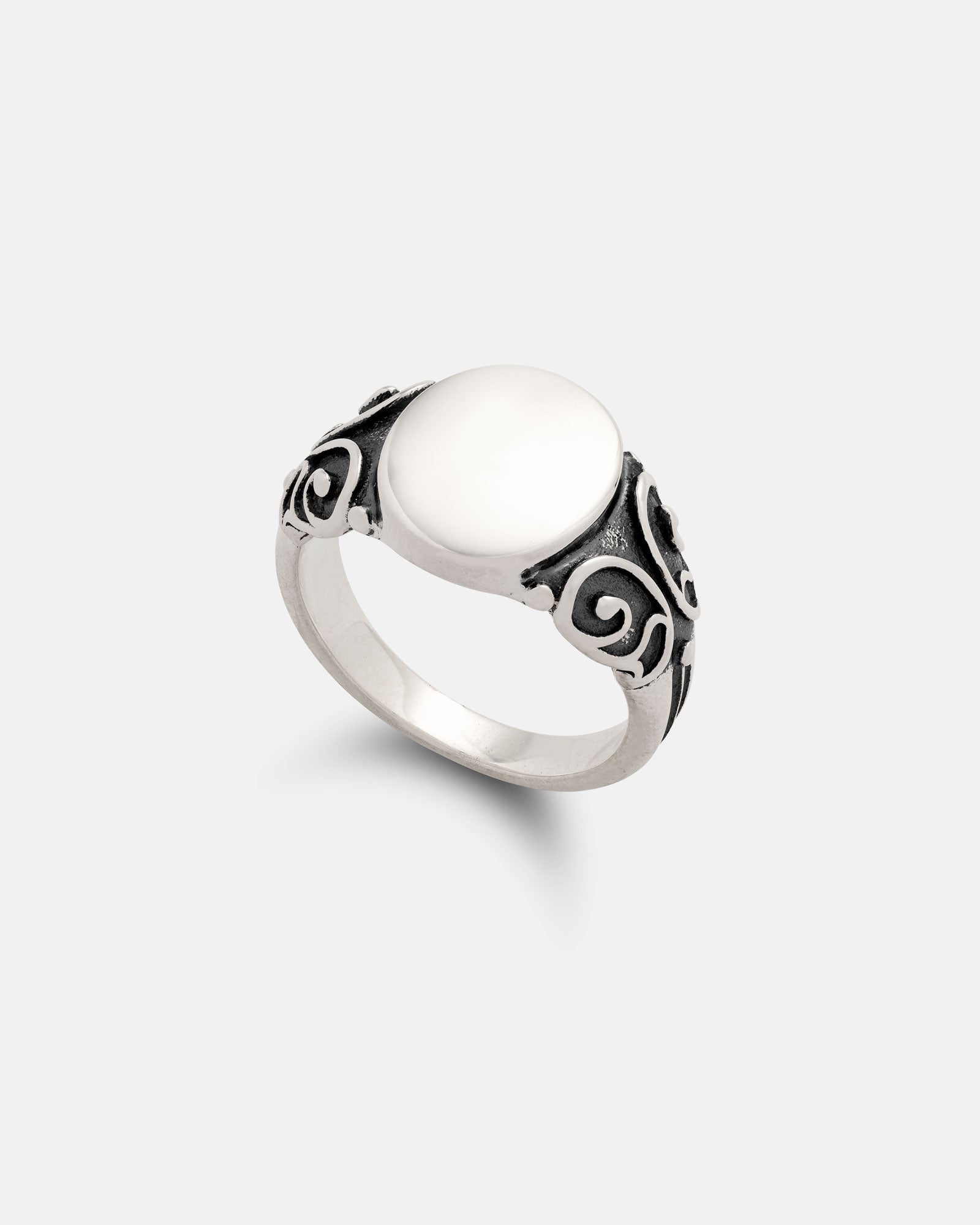 The 925 Sterling Silver Mini Oval Scroll Signet Ring features decorative blackened scrollwork on both sides of the band and a smooth white stone at its center, shown against a plain light background.