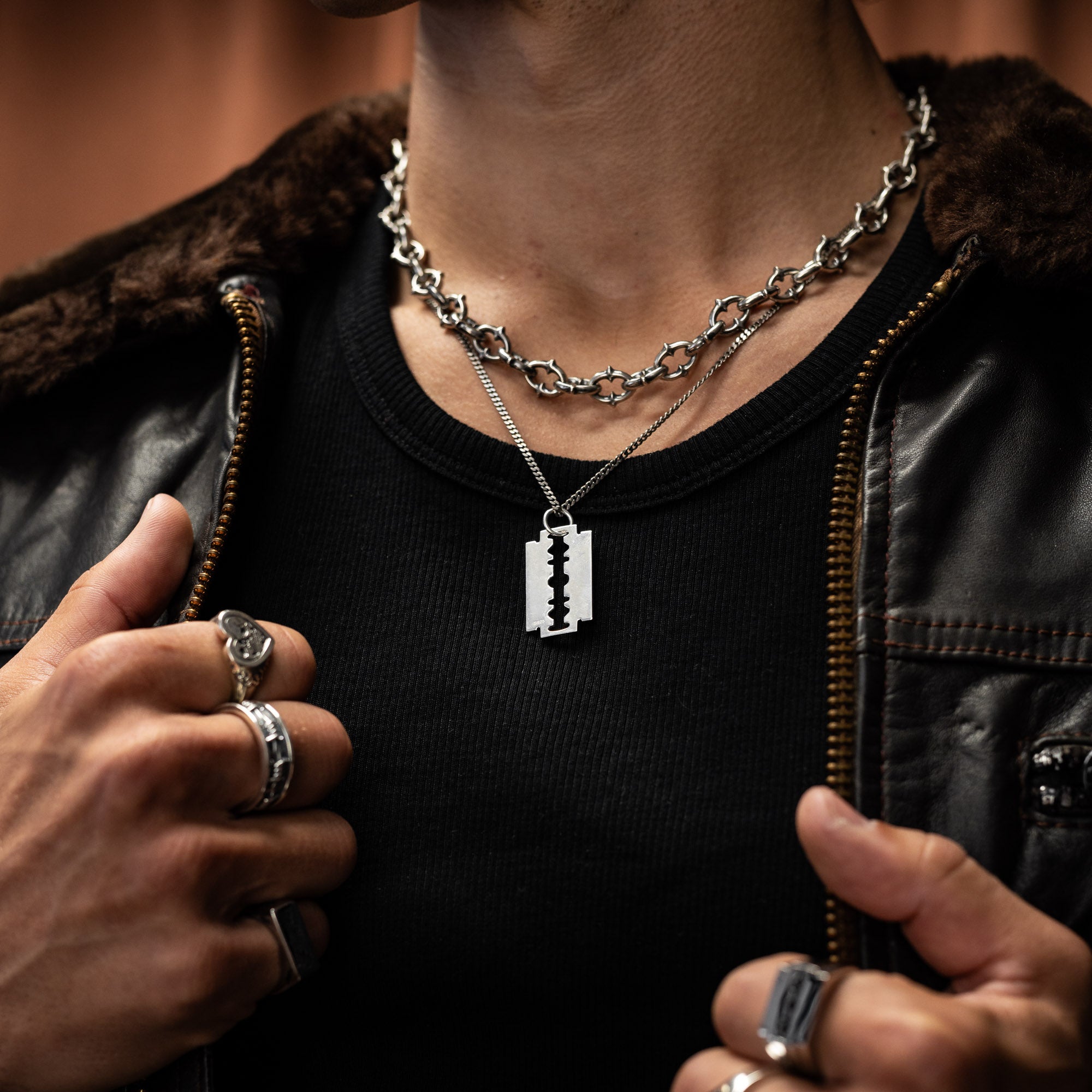 Person wearing a black leather jacket and black shirt with a silver chain necklace and razorblade pendant in 925 sterling silver