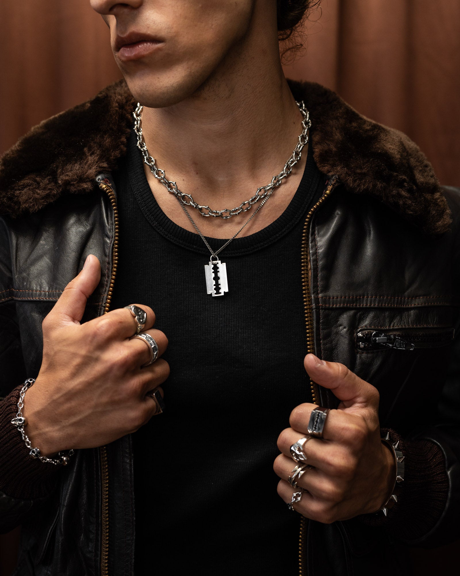 Man wearing a black leather jacket with fur collar, black shirt, and multiple sterling silver necklaces and rings.