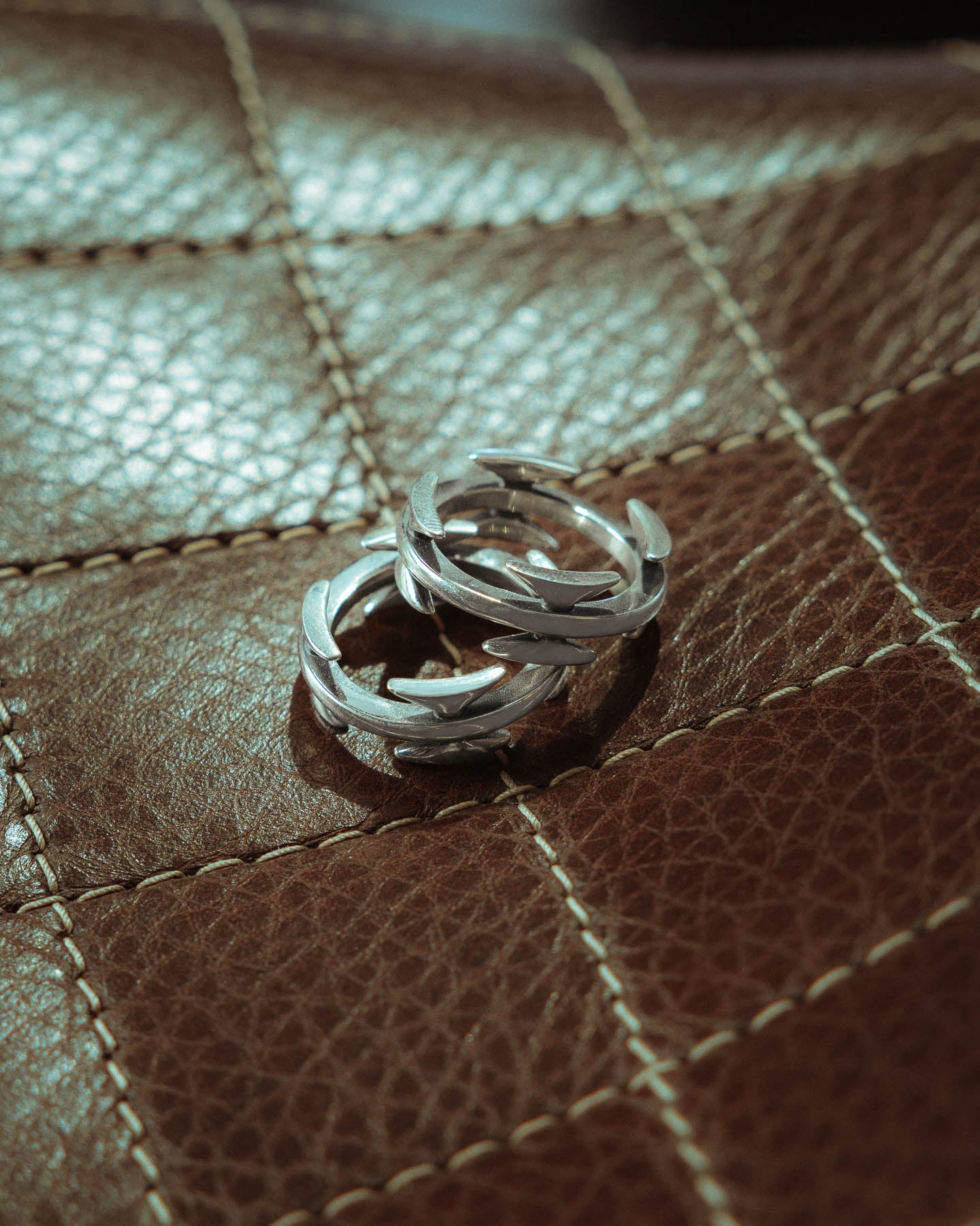 Two 925 Sterling Silver Razor Wire Rings with a tattoo-inspired design sit on a brown stitched leather surface, bathed in soft natural light.