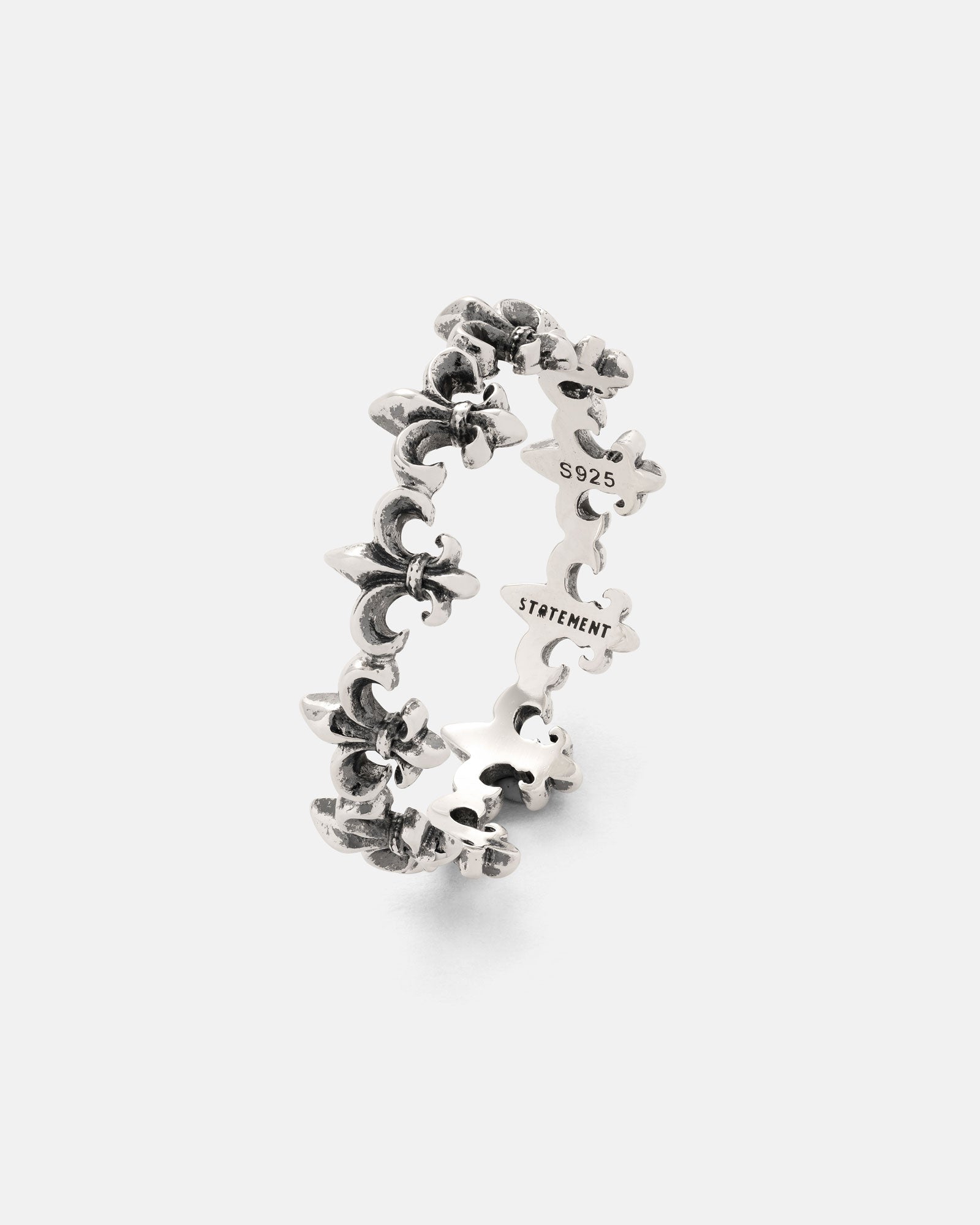 The 925 Sterling Silver “Fleur De Lis” Ring from Statement Collective is crafted in antique silver and features a repeating fleur-de-lis pattern encircling the band. Engraved with STATEMENT and an S925 mark on the inside, this ring is presented against a plain white background.