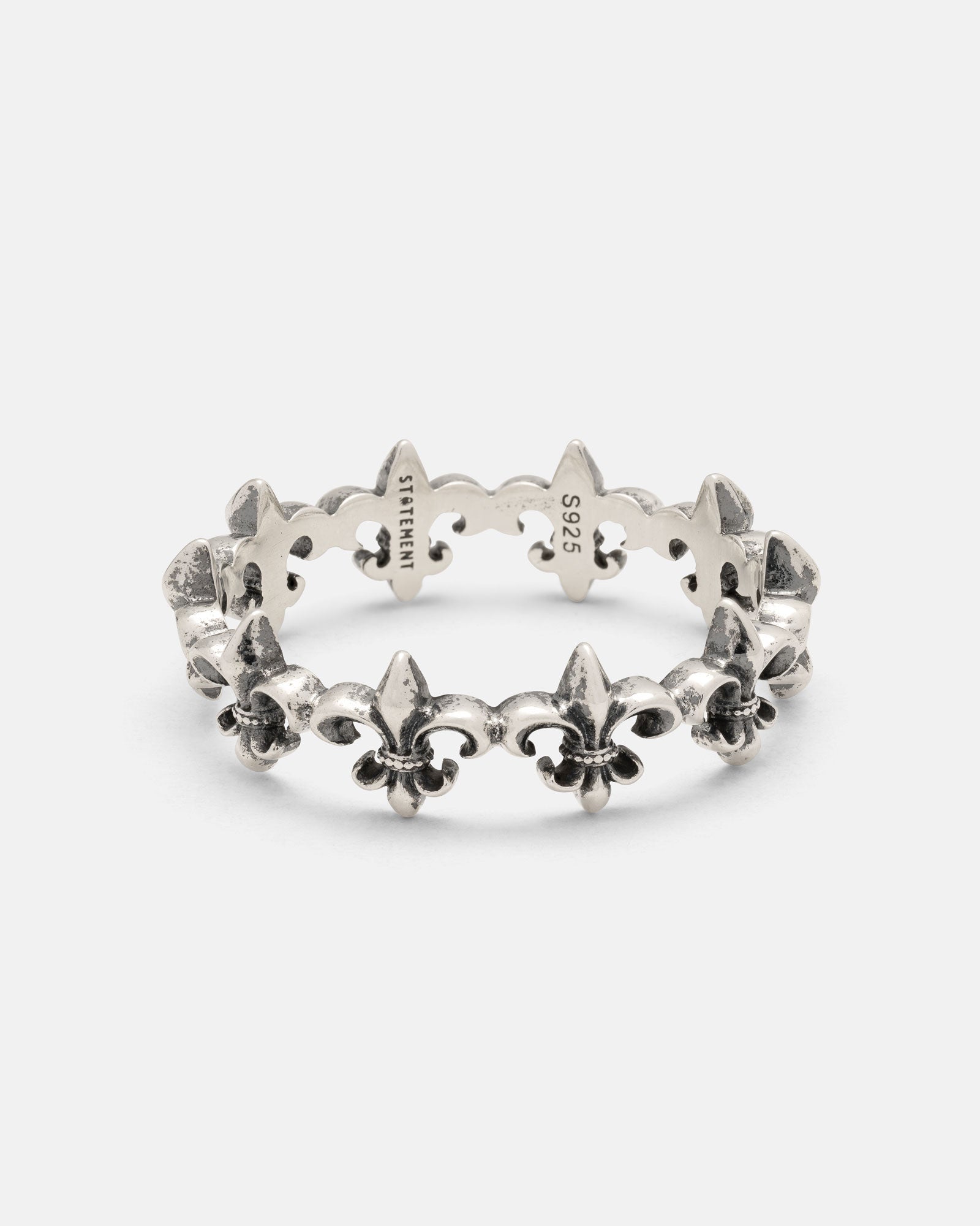 The Statement Collective 925 Sterling Silver “Fleur De Lis” Ring features a repeating fleur-de-lis pattern encircling the band, with engraved STERLING and 925 markings on the inner side. This elegant ring embodies timeless design and classic craftsmanship.