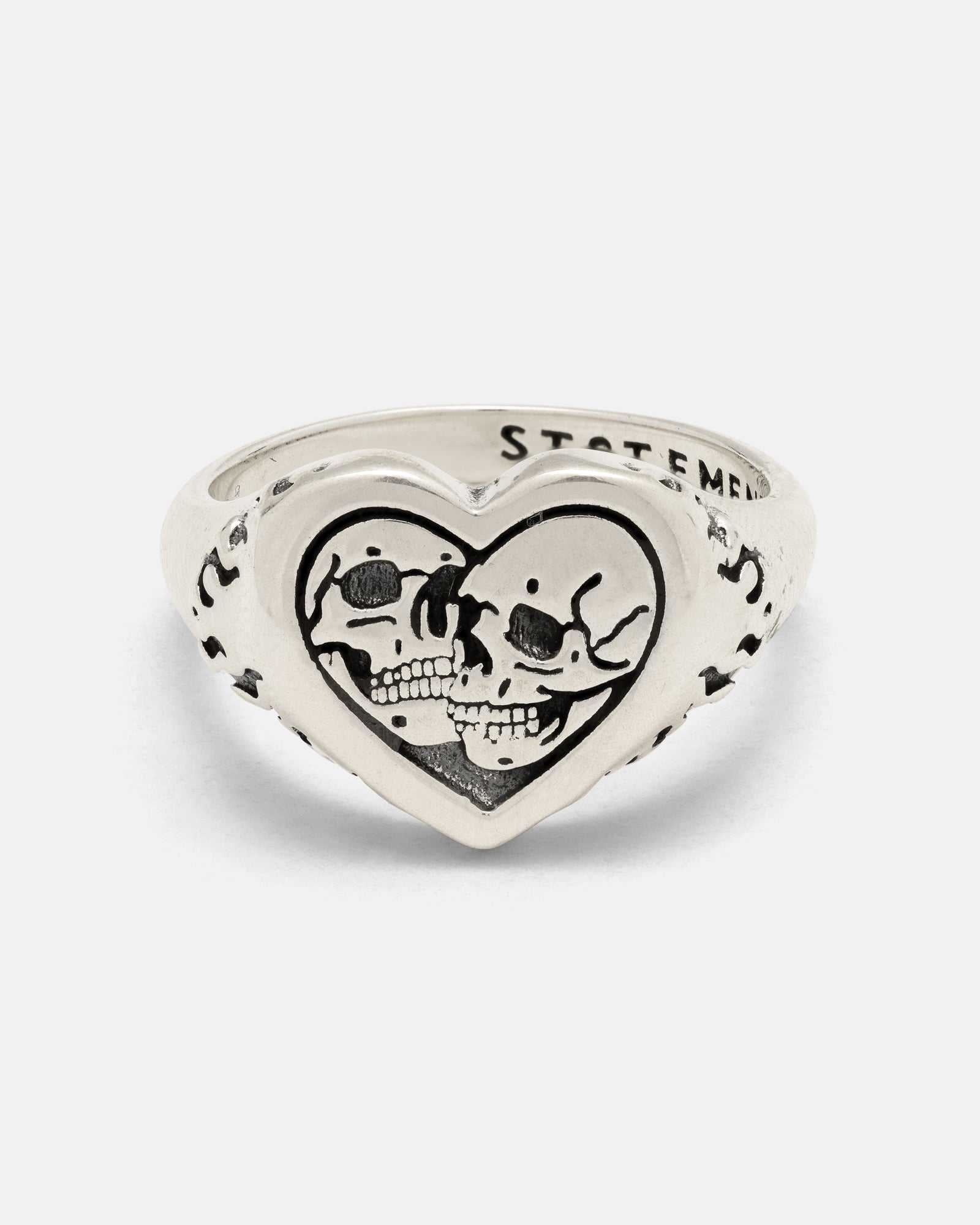 The 925 Sterling Silver Skull Heart Ring by Statement Collective showcases two skulls facing one another within a heart-shaped frame, enhanced by engraved details along the band—this handcrafted piece of silver jewelry combines edgy style with intricate artistry.