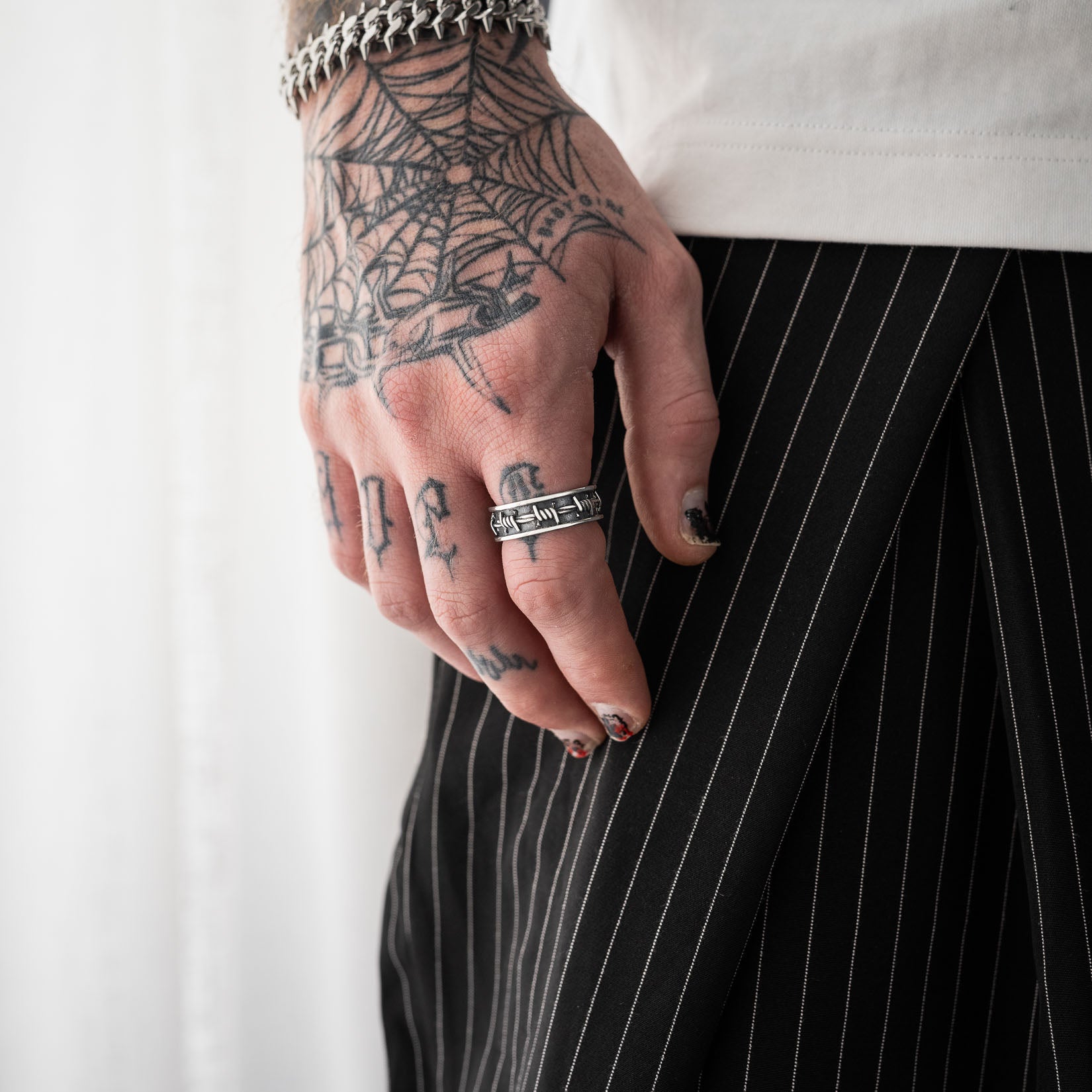 Hand with tattoos wearing a barbed wire band ring in sterling silver against a white background
