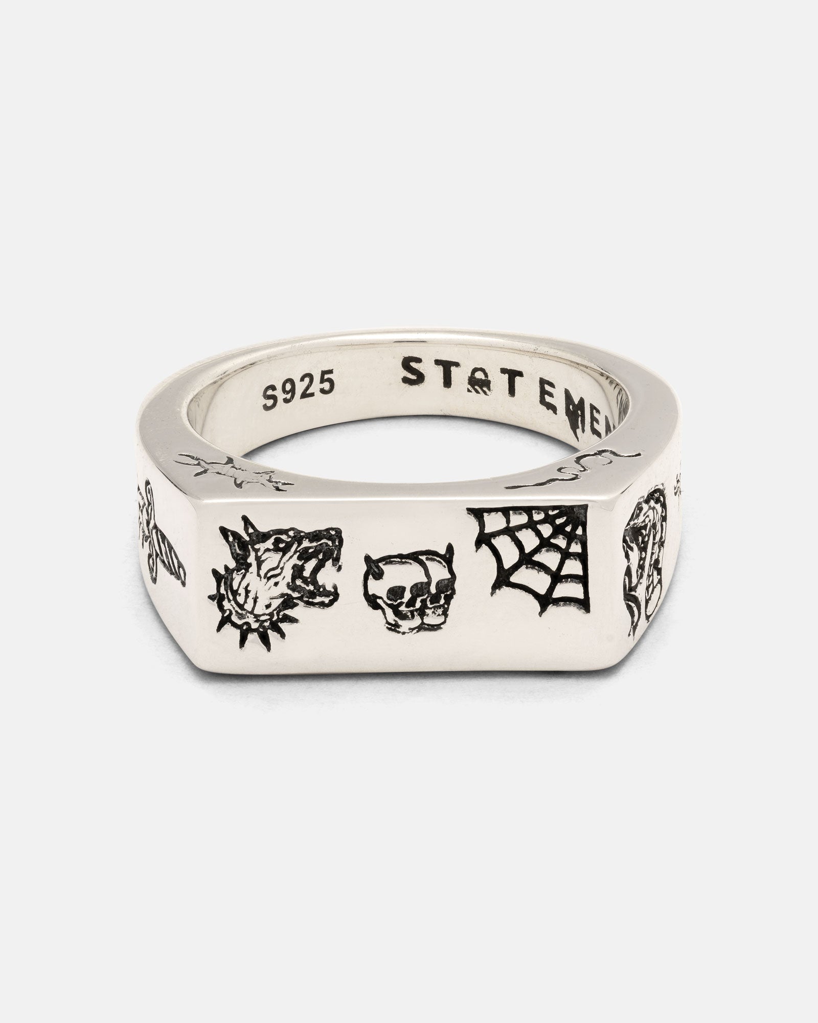 Introducing the Statement Collective 925 Sterling Silver Tattoo Signet Ring—a silver square signet ring engraved with black patchwork tattoo designs, featuring a wolf head, skull, spider web, and other small symbols. Crafted from 925 sterling silver, the inner band is stamped with “S925” and “STATEMENT.”.