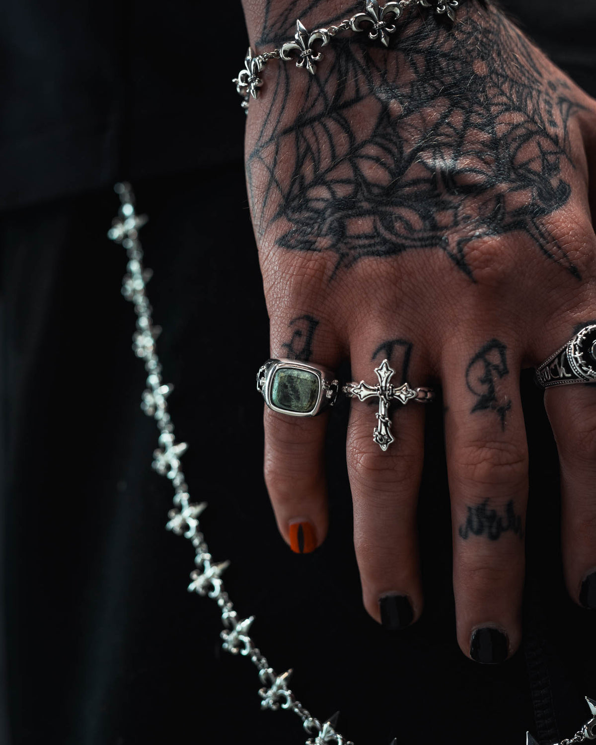 A hand adorned with spiderweb tattoos, black nail polish, and Statement Collective’s 925 Sterling Silver Kambaba Jasper Stone Ring creates a striking look. Paired with silver cross rings, razor wire-inspired jewelry, and a silver chain with cross charms layered over black clothing, the edgy sterling silver aesthetic is perfectly complete.