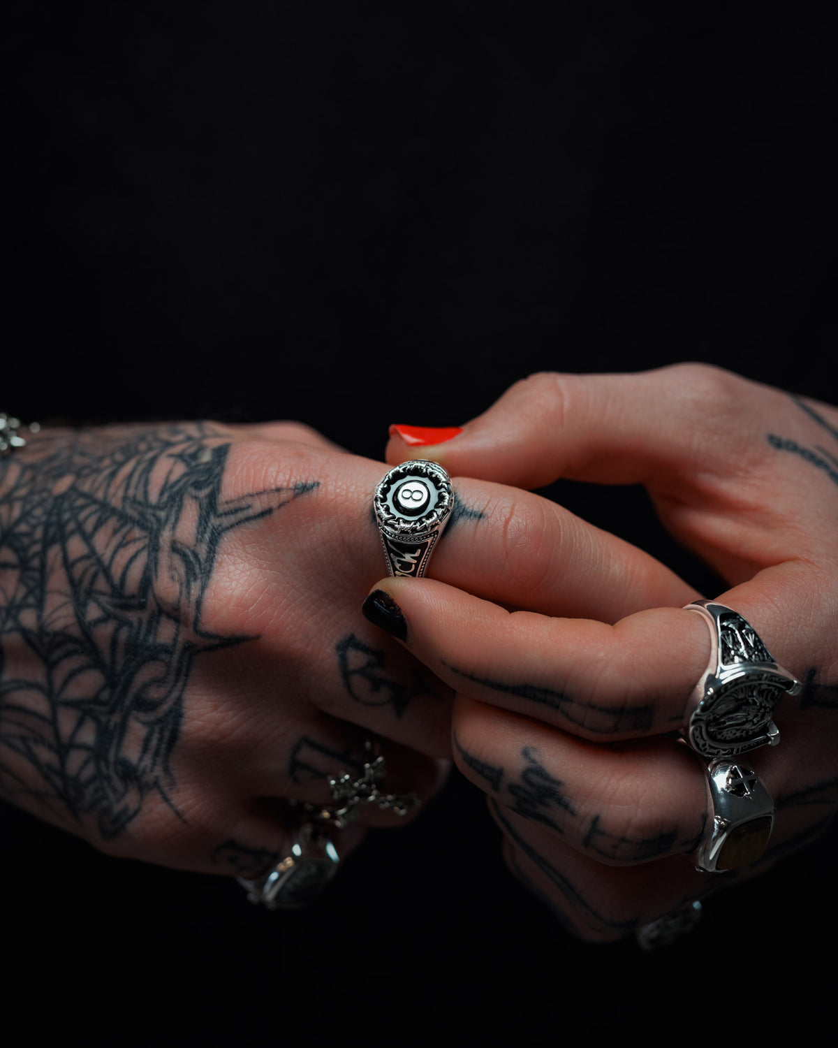 Tattooed hands wearing silver rings, one hand adjusting the Statement Collective 925 Sterling Silver Lucky Shot Ring with a dark circular design on the other hand’s finger, set against a dark background.