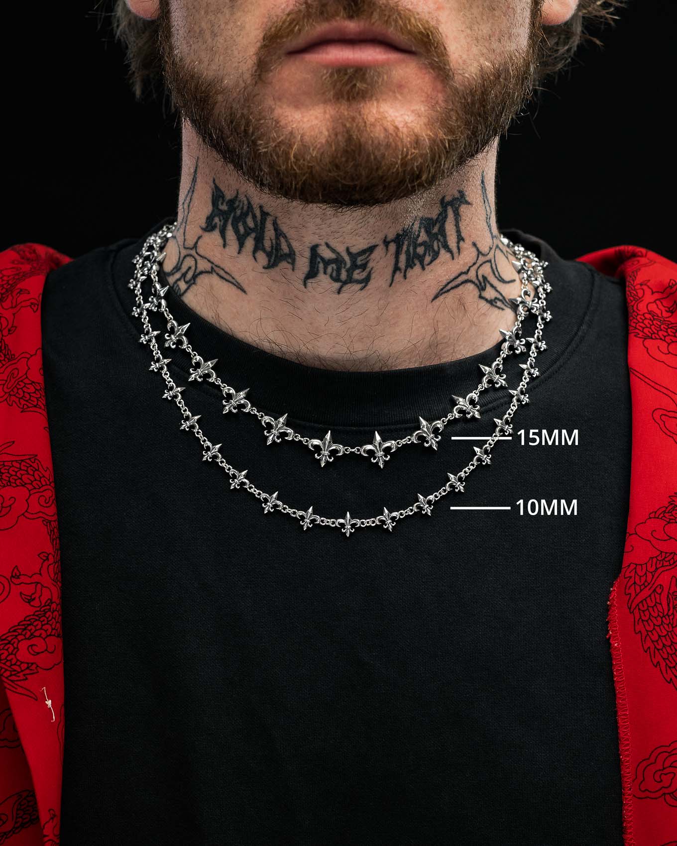 A man with a neck tattoo wears two silver chains of different thicknesses, including the Statement Collective 925 Sterling Silver “Fleur De Lis” 10mm Chain, over a black shirt and a red jacket featuring a dragon design on the sleeves.