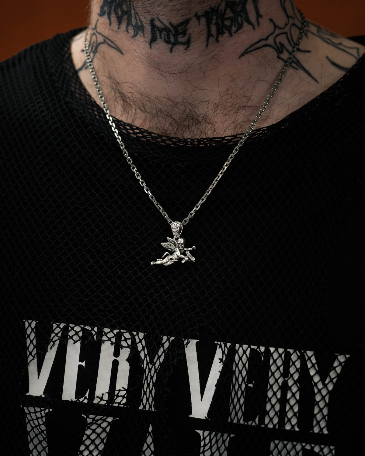 man with neck tattoo wearing sterling silver cherub pendant against dark orange background