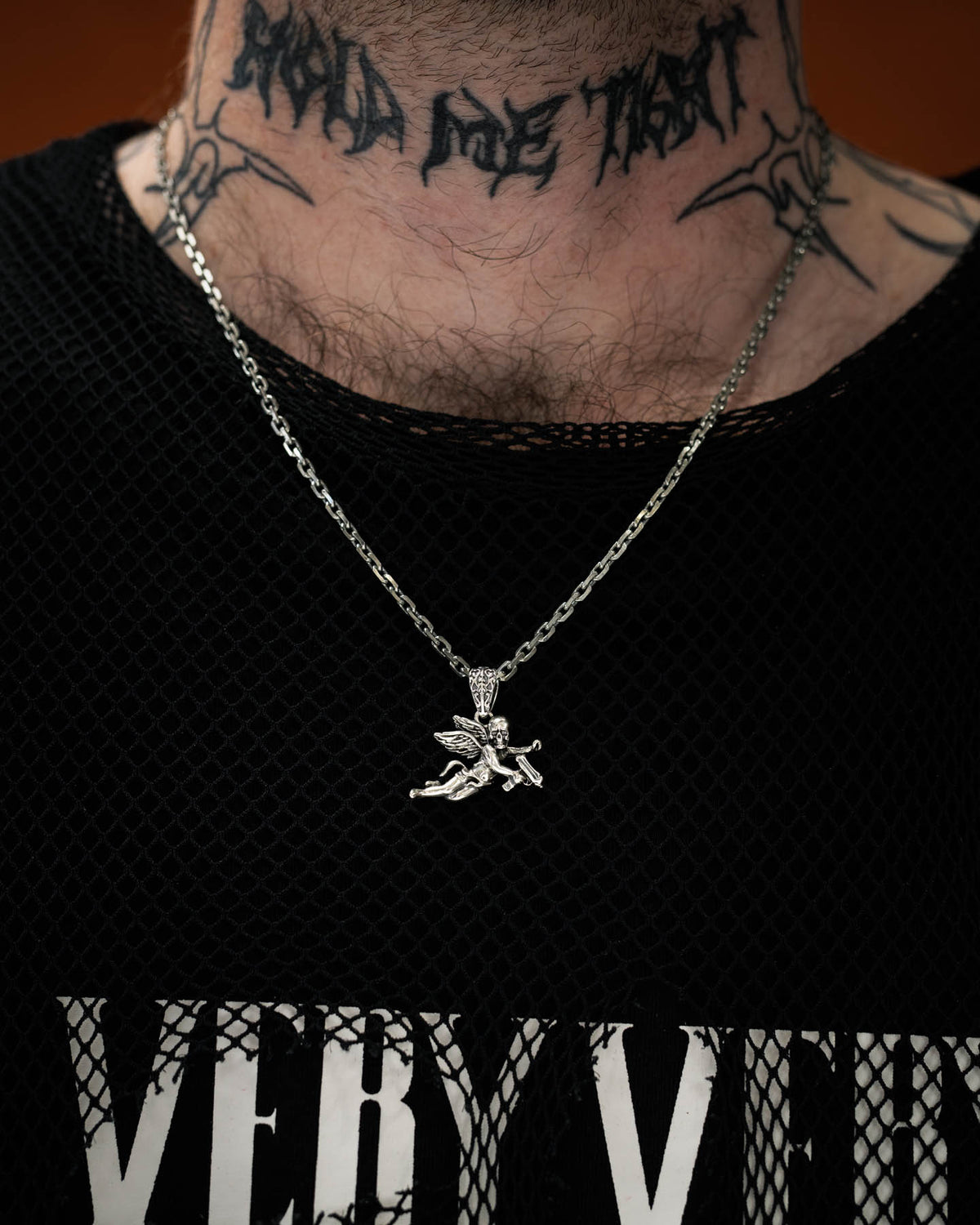 man with neck tattoo wearing sterling silver cherub pendant against dark orange backdrop