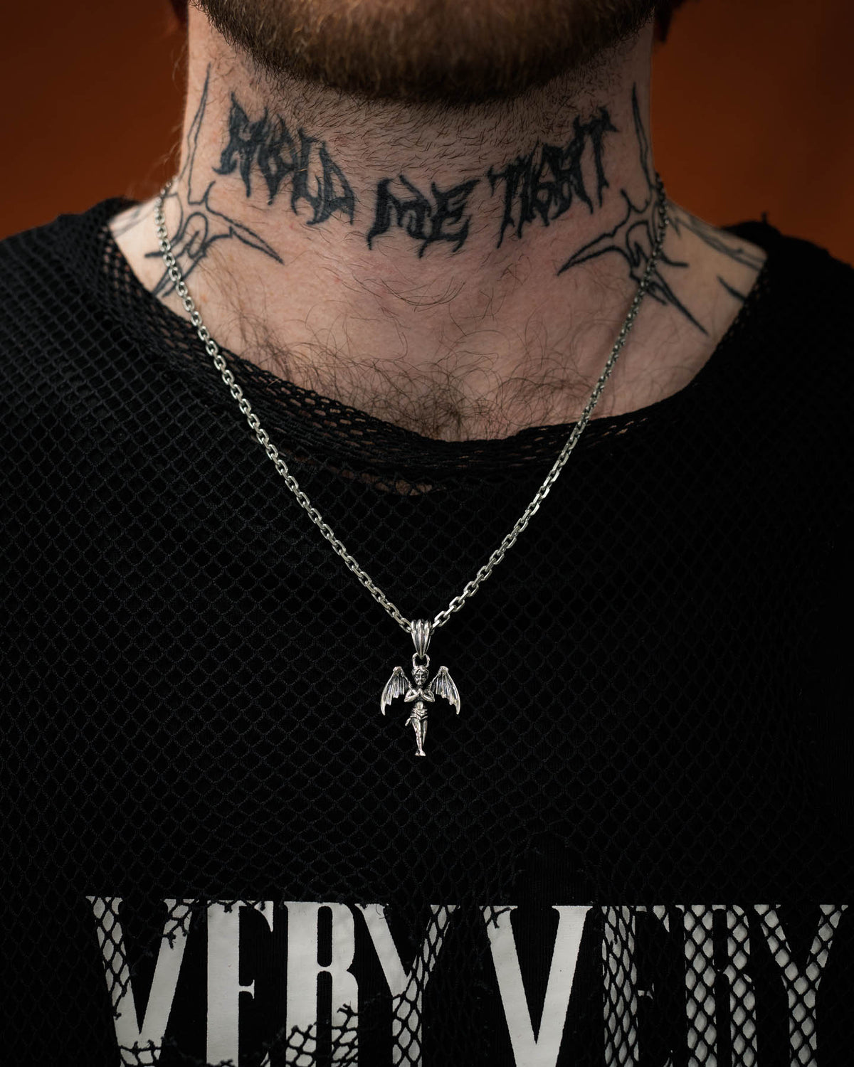 tattooed model wearing 925 silver cherub pendant with devil wings against orange backdrop