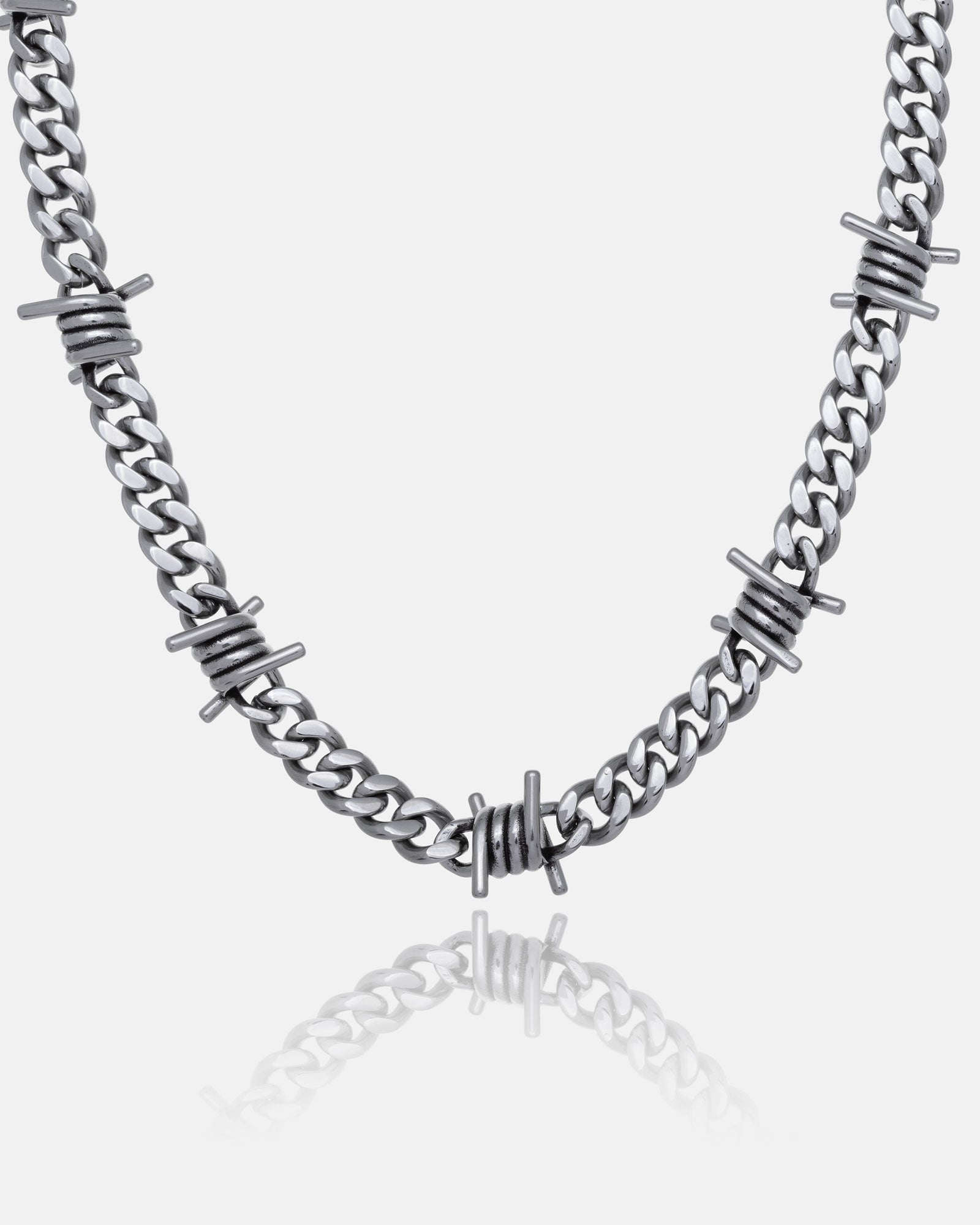 The 9mm Barbed Wire Cuban Chain features barbed wire-inspired accents along its silver links, showcased on a white background with a subtle reflection.
