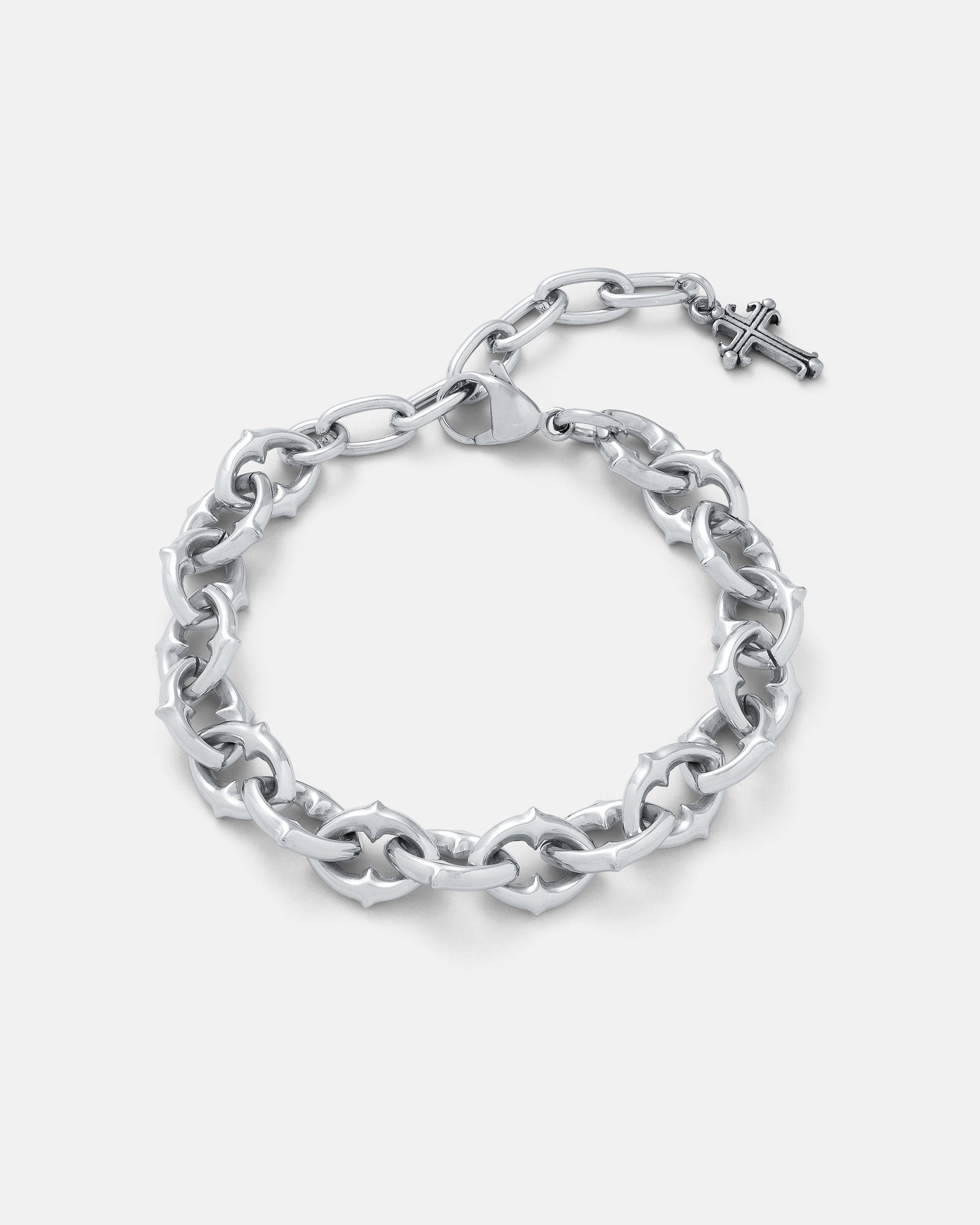 9mm Spiked chain link bracelet with 5cm extender chain finished off with a dangling cross charm in silver by statement collective on light grey background.