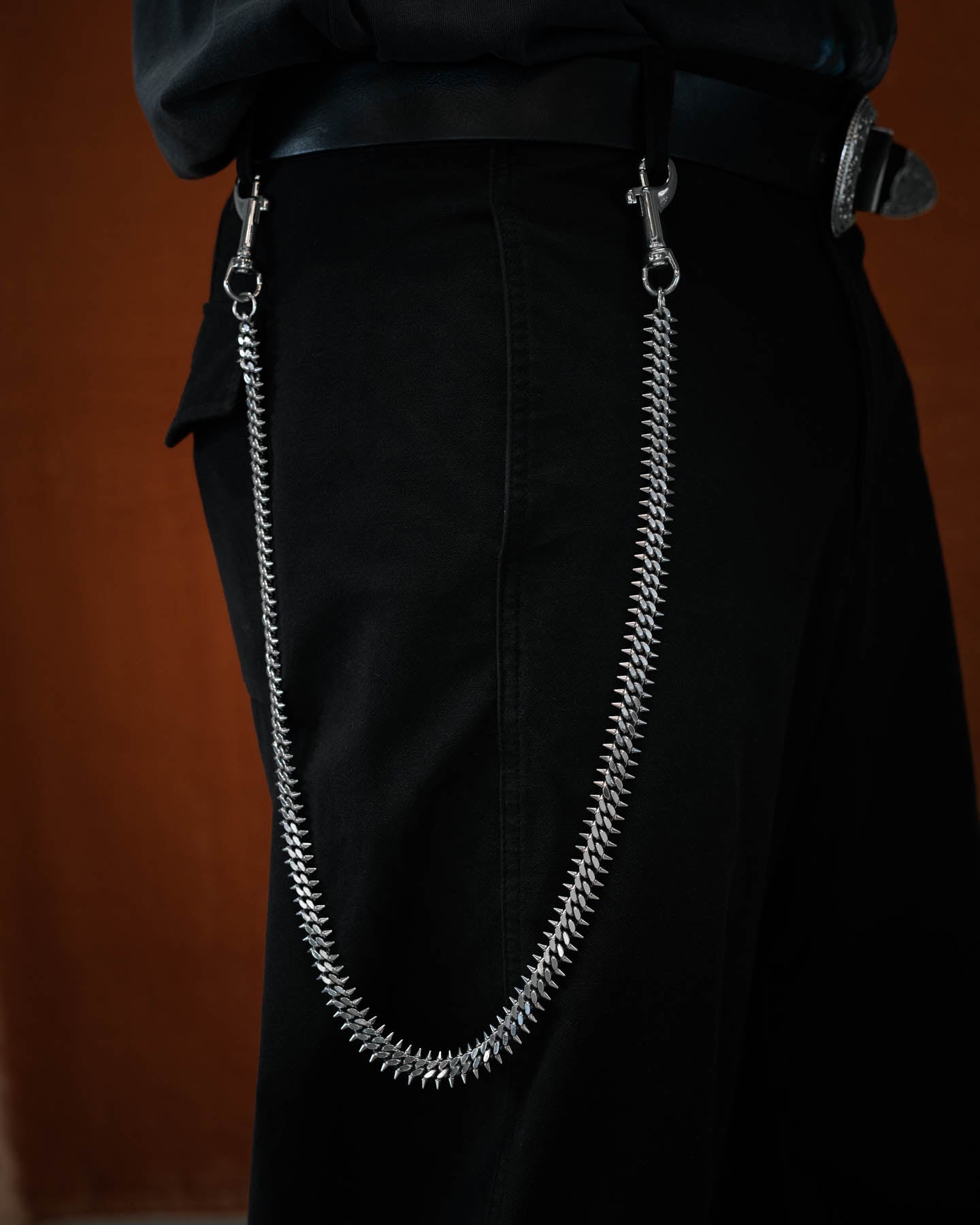 silver spiked cuban wallet chain on model with black pants against orange background