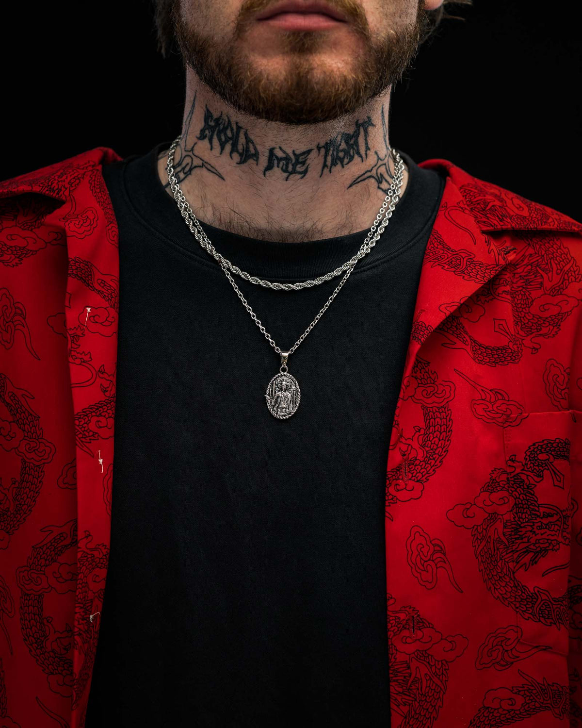 A person wearing a red patterned shirt over a black t-shirt, layered silver chains with the STATEMENT “Big Iron” Pendant, and a neck tattoo. The image is cropped just below the nose.