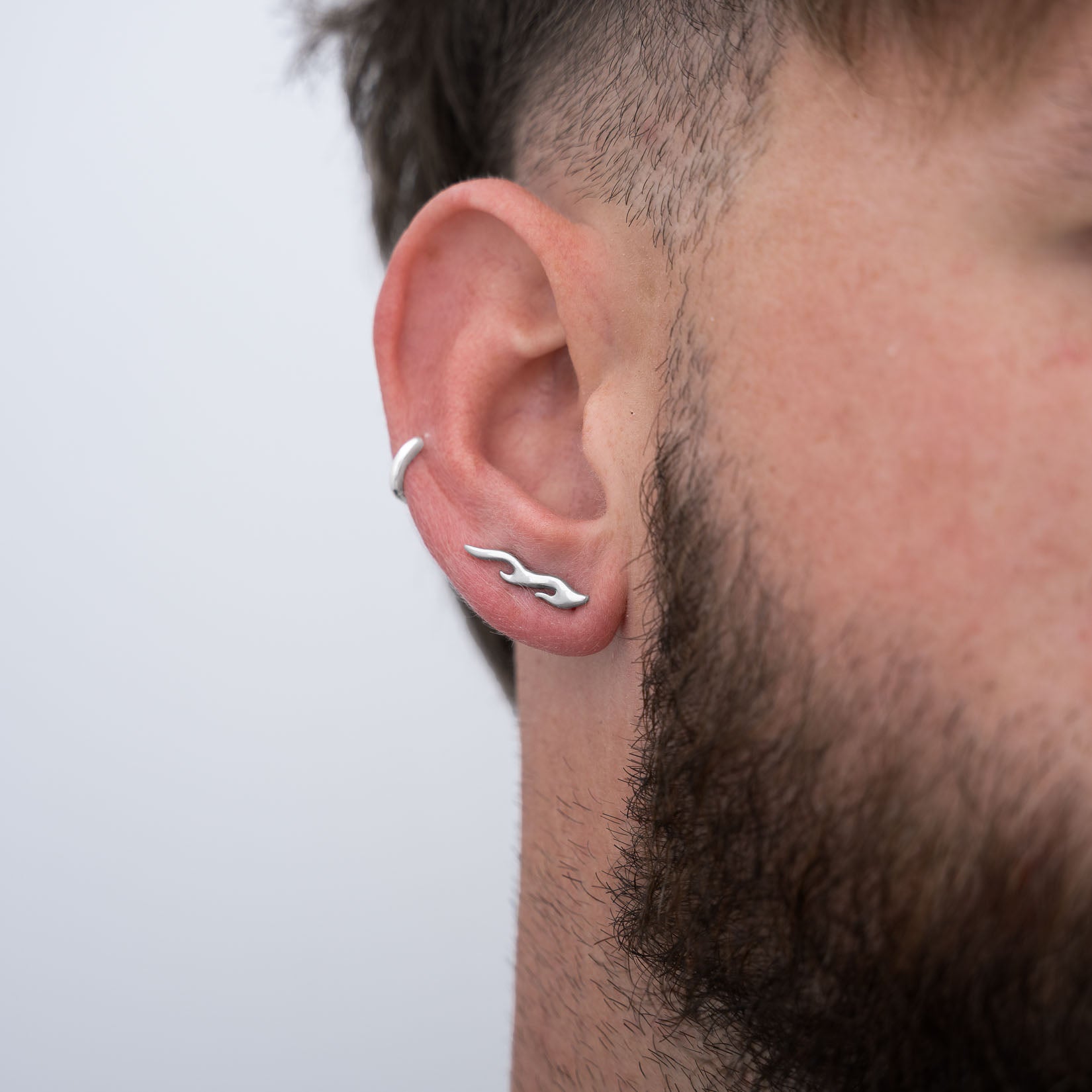 Close-up of a man's right ear with a silver flame earring on a light gray background