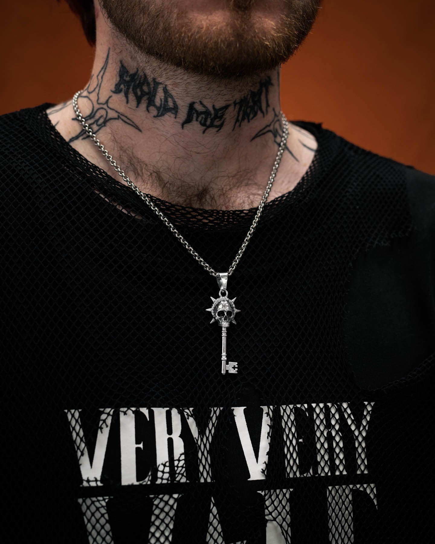 Silver key-shaped pendant with skull design on a chain on tattooed model's neck