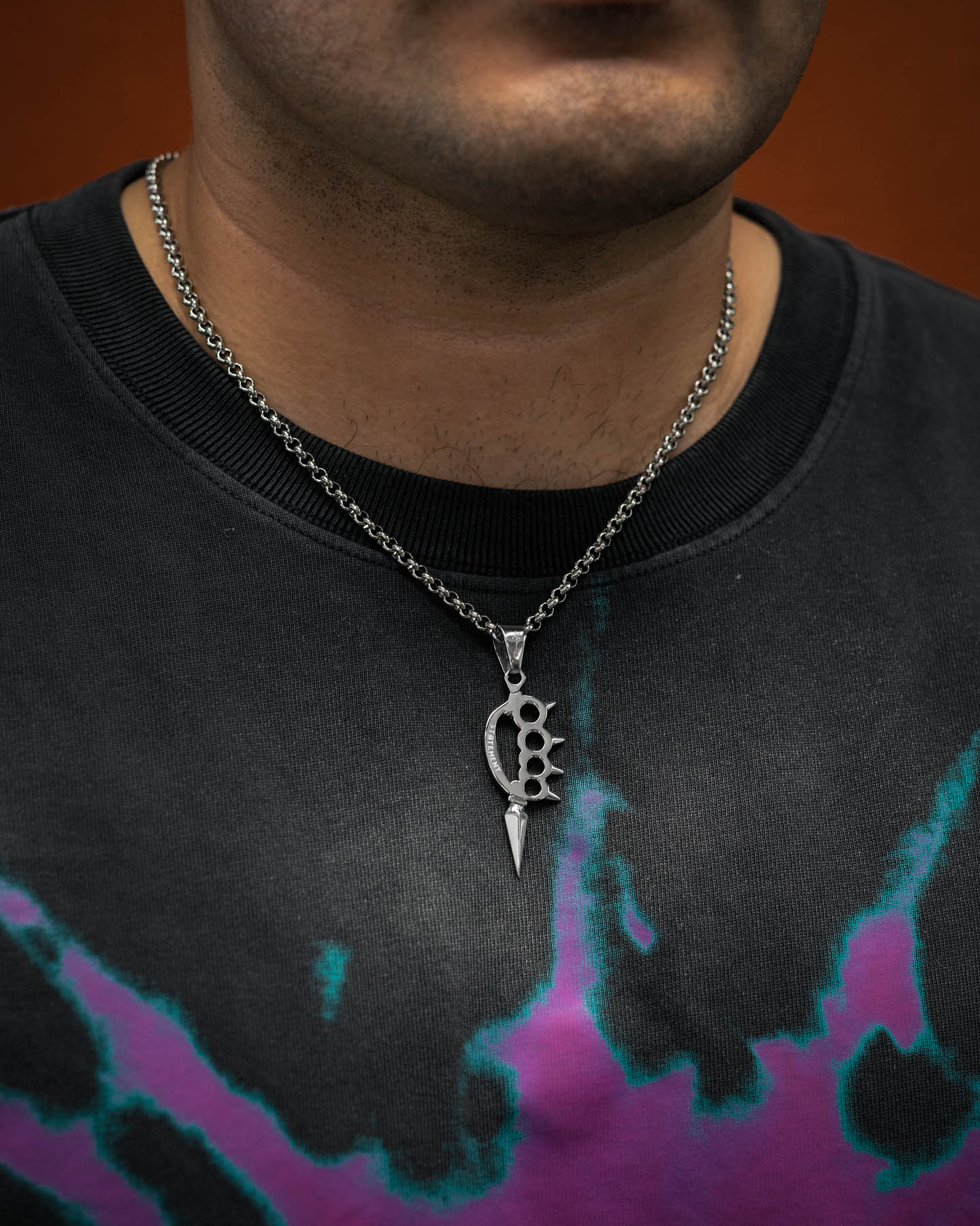 Silver knuckle duster pendant with long spike on a chain on model's neck