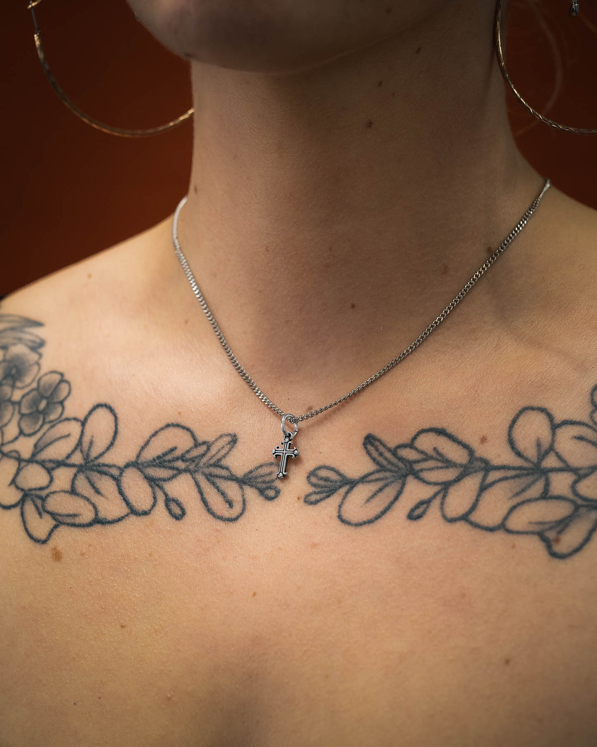 mini french cross pendant in 316L stainless steel on tattooed female model's neck against orange backdrop